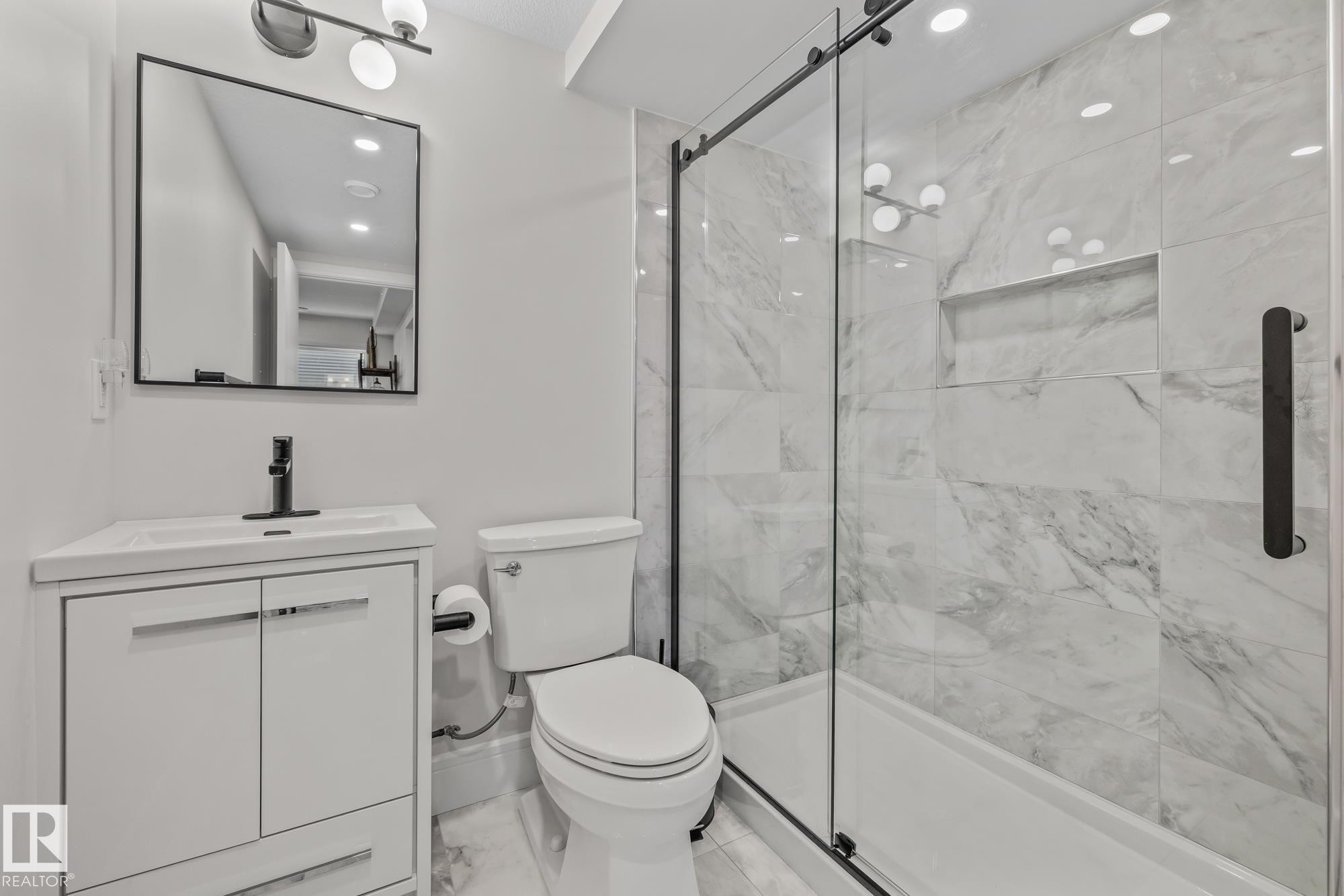 Bathroom featuring a white vanity with a rectangular sink, a black framed mirror, and a walk-in shower with a glass enclosure and marble-style tiling - 3864 Robins Crescent, Edmonton, AB - Indoor Photo Showing Bathroom