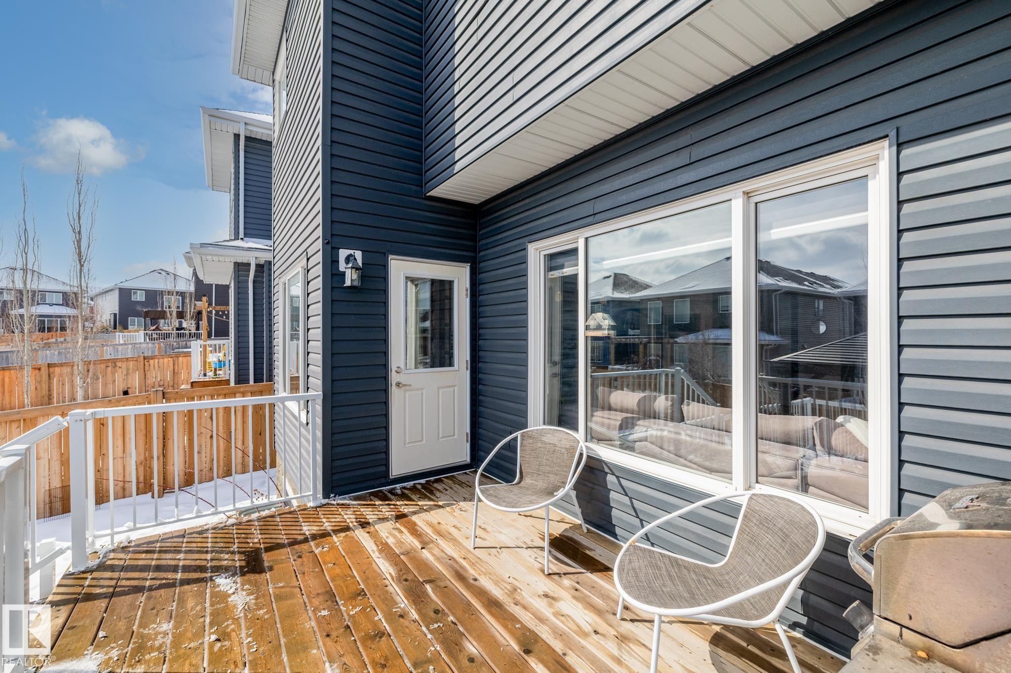 The property features a wooden deck with white railings, a blue exterior with white trim, and a window and door providing access to the interior - 3864 Robins Crescent, Edmonton, AB - Outdoor With Deck Patio Veranda