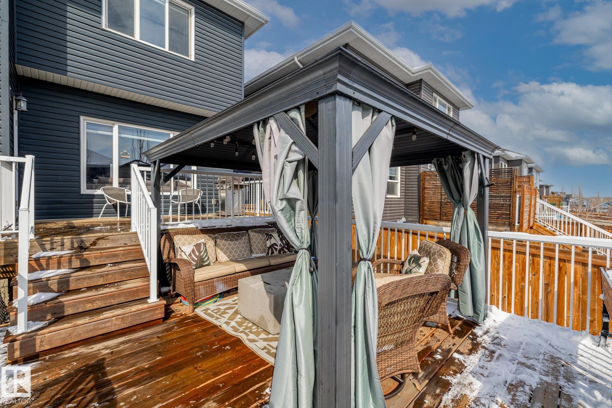Outdoor deck featuring a dark gazebo with curtains and a seating area, alongside a white railing and wooden stairs - 3864 Robins Crescent, Edmonton, AB - Outdoor With Deck Patio Veranda With Exterior