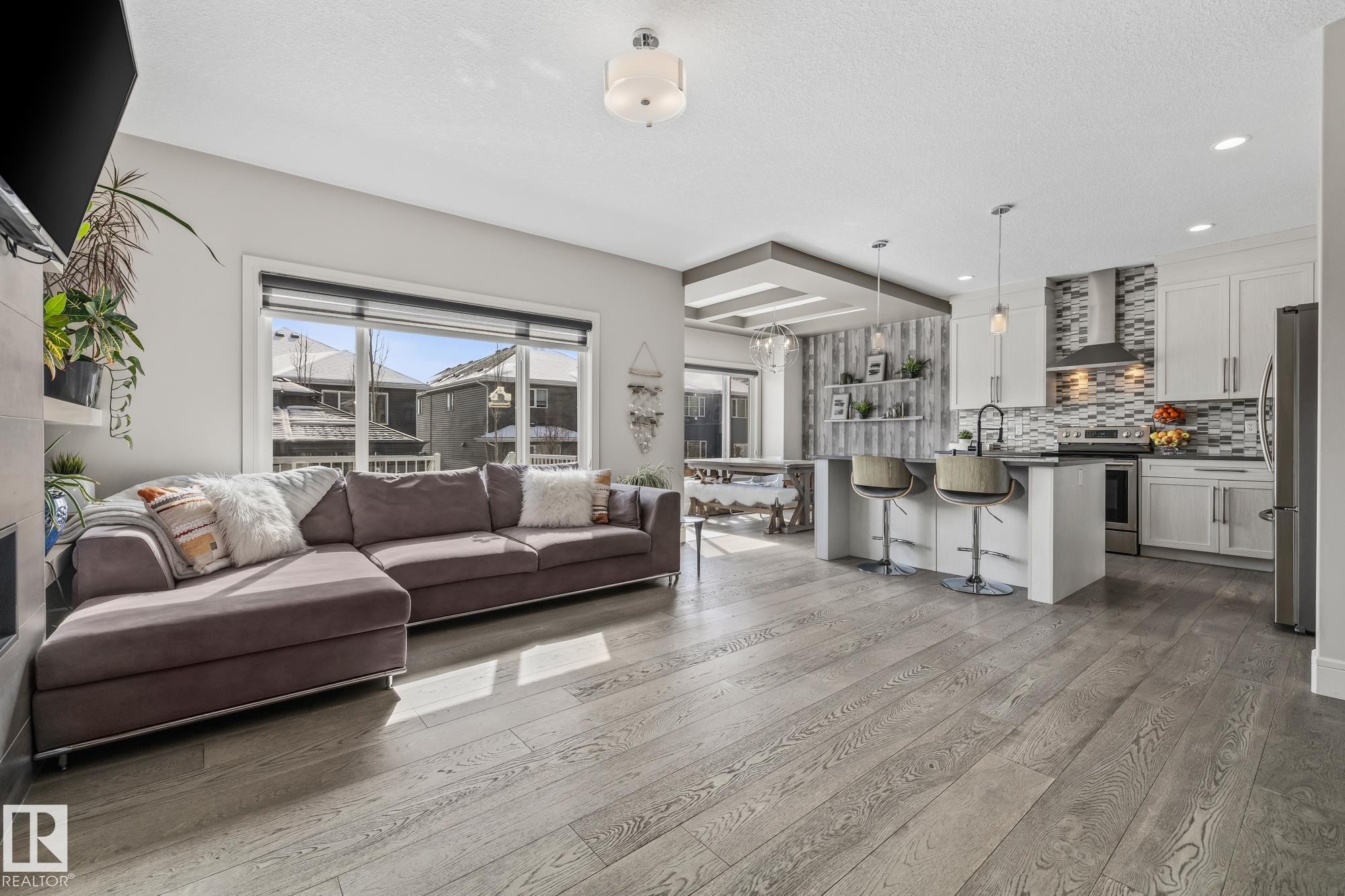 Open concept living space featuring wide plank flooring, a kitchen with white cabinetry, a large island with seating, and stainless steel appliances - 3864 Robins Crescent, Edmonton, AB - Indoor