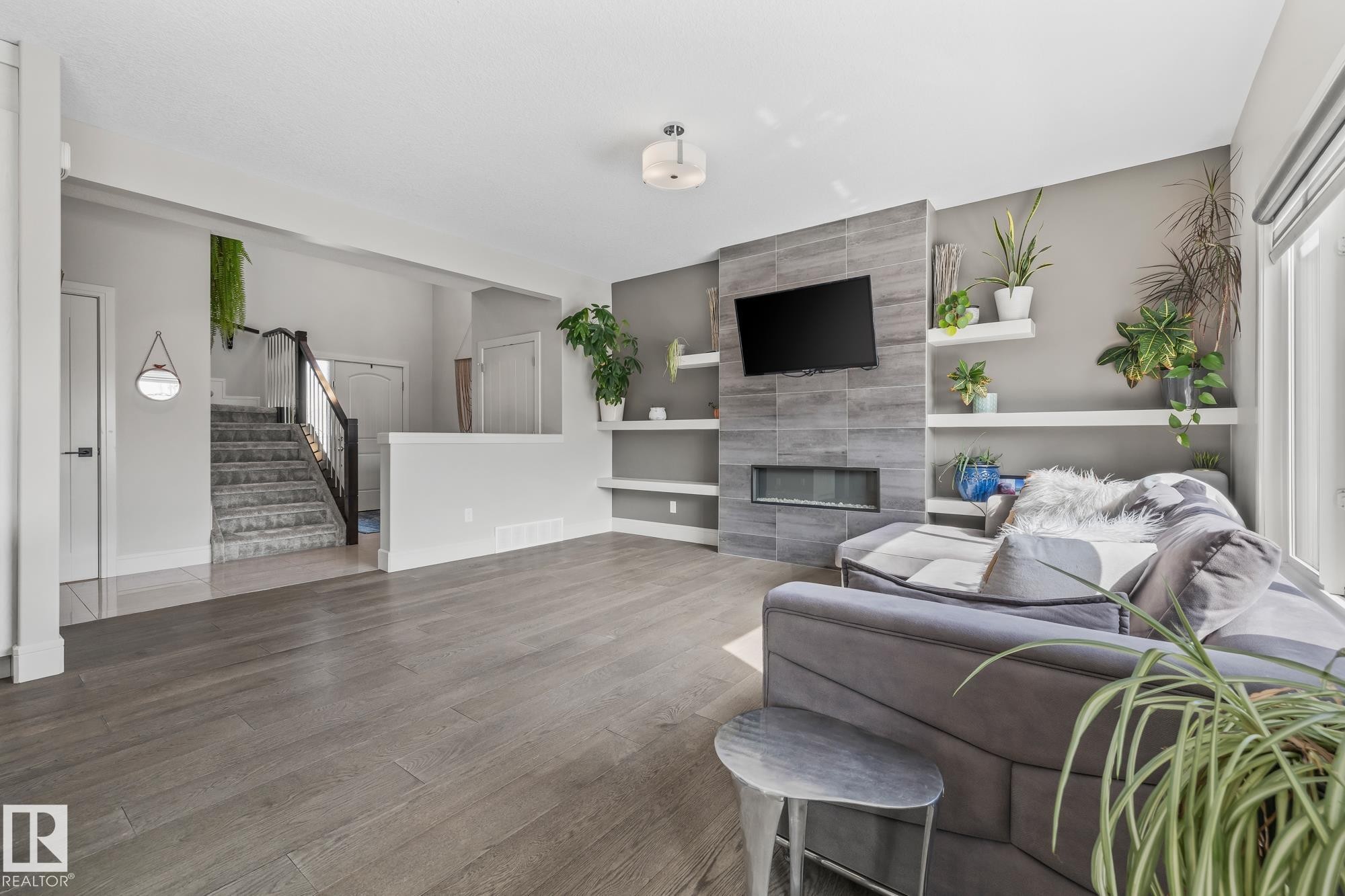 The living room features hardwood flooring, a tiled fireplace with an integrated television, and built-in shelving - 3864 Robins Crescent, Edmonton, AB - Indoor Photo Showing Living Room With Fireplace