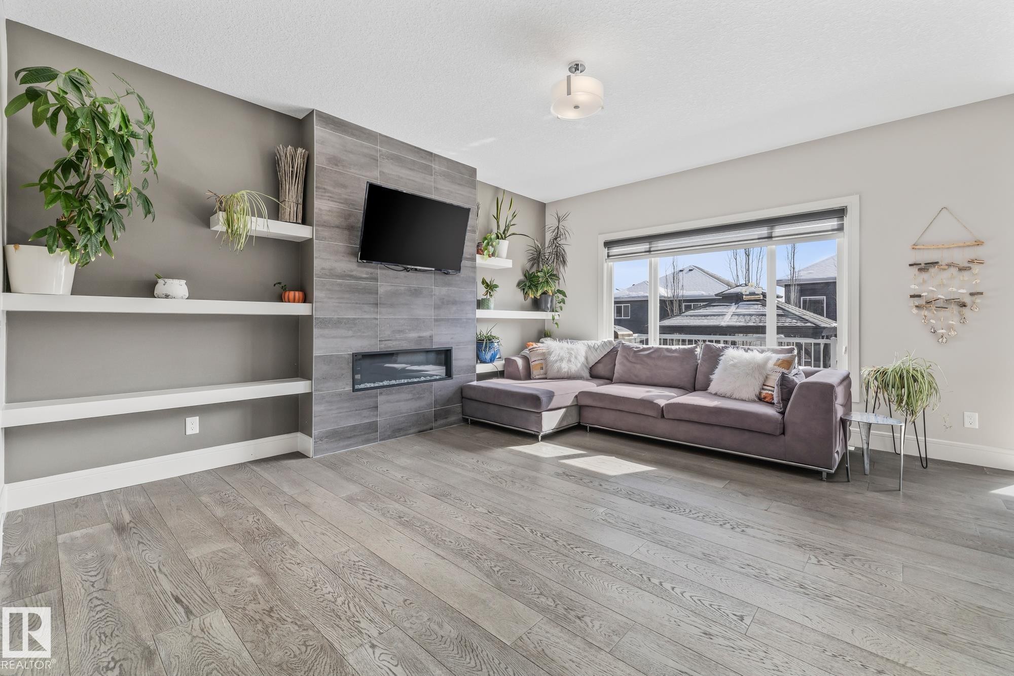 Living area featuring light hardwood floors, built-in shelving, and a modern fireplace with a tiled surround - 3864 Robins Crescent, Edmonton, AB - Indoor Photo Showing Living Room With Fireplace