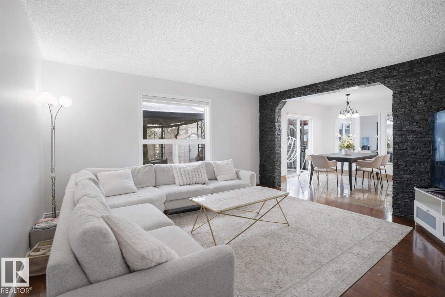 Living room featuring light-colored walls and dark hardwood flooring, with a window providing outdoor views - 4619 202 Street, Edmonton, AB - Indoor Photo Showing Living Room