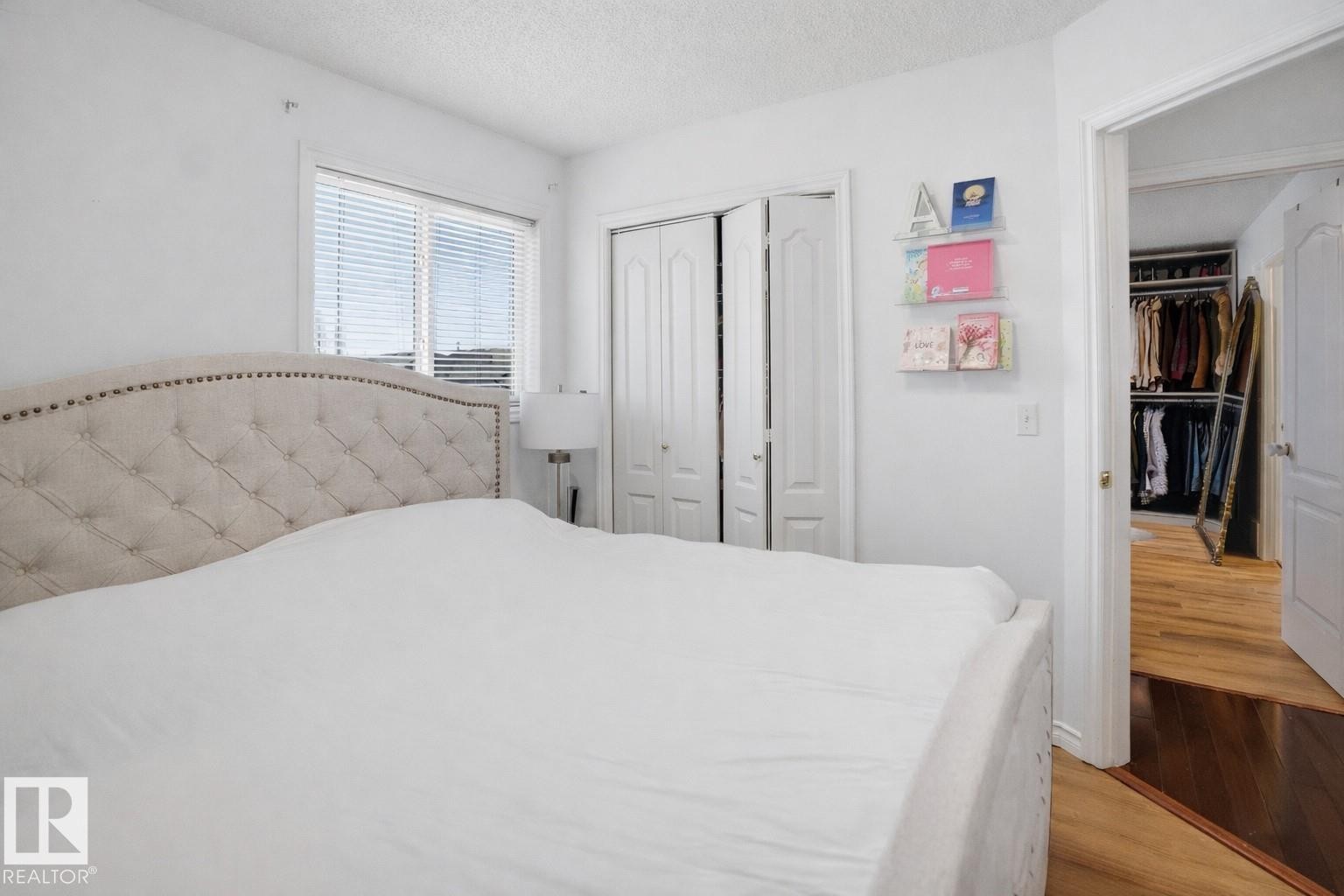 This bedroom features a window with blinds, bi-fold closet doors, and hardwood flooring visible through the doorway - 4619 202 Street, Edmonton, AB - Indoor Photo Showing Bedroom