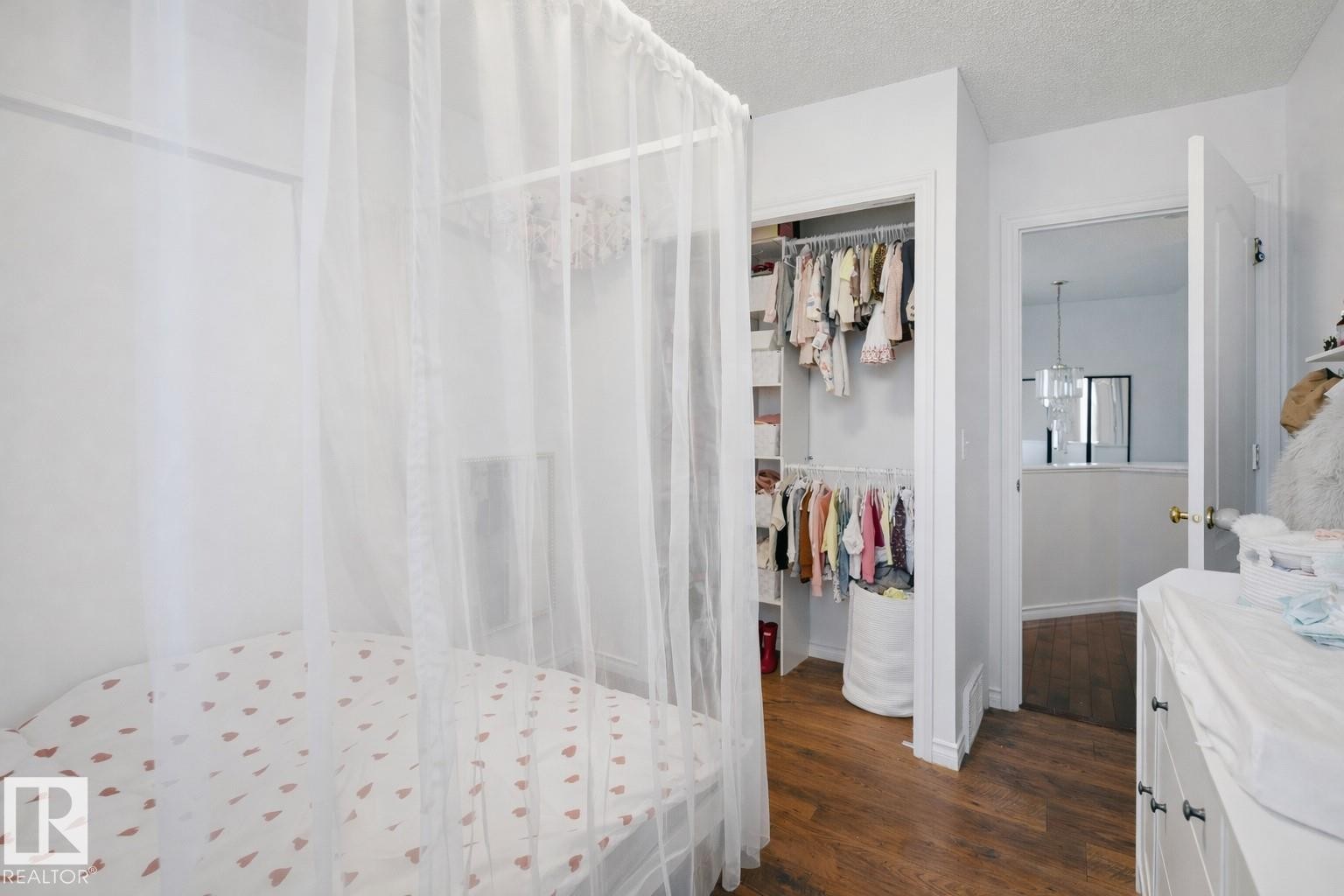 This room features light-toned walls, rich wood-style flooring, and an open closet space with built-in shelving - 4619 202 Street, Edmonton, AB - Indoor Photo Showing Bedroom