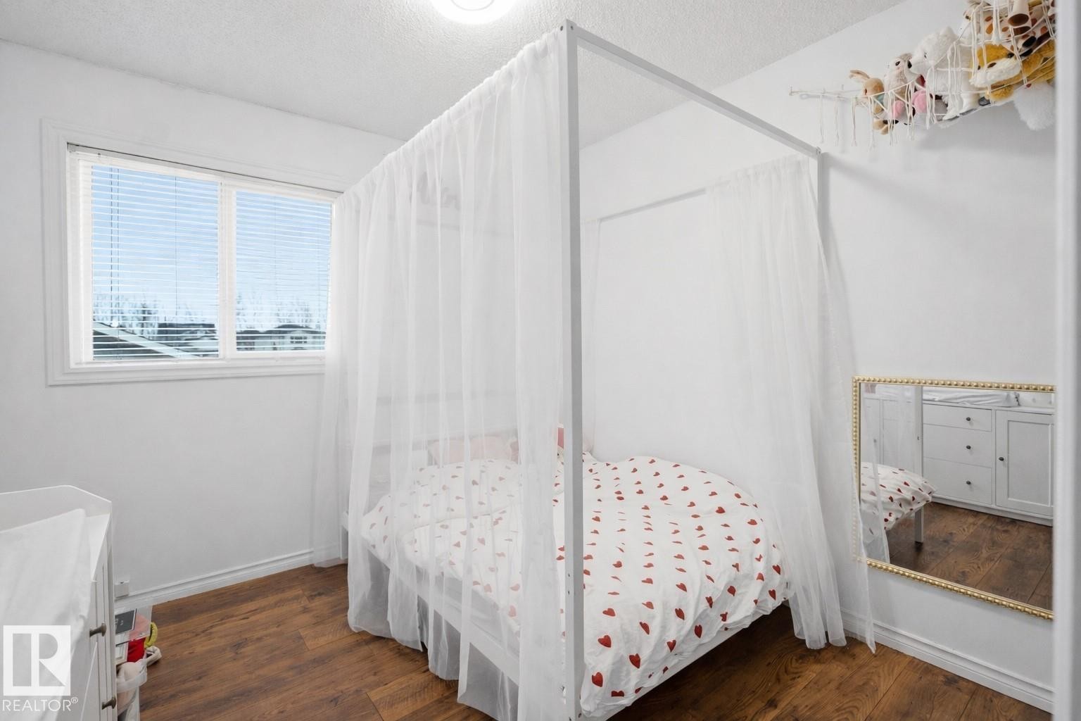 The room features warm-toned hardwood flooring and a window with blinds providing natural light - 4619 202 Street, Edmonton, AB - Indoor Photo Showing Bedroom