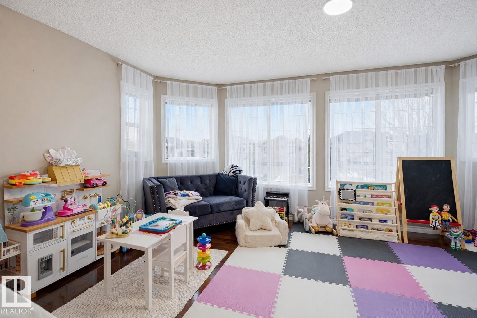 This versatile room features multiple windows with sheer curtains, providing ample natural light - 4619 202 Street, Edmonton, AB - Indoor