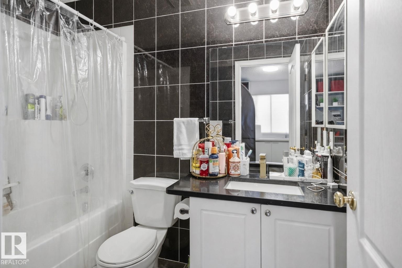 Bathroom featuring dark tiled walls, a white vanity with a dark countertop, and a shower-bathtub combination - 4619 202 Street, Edmonton, AB - Indoor Photo Showing Bathroom