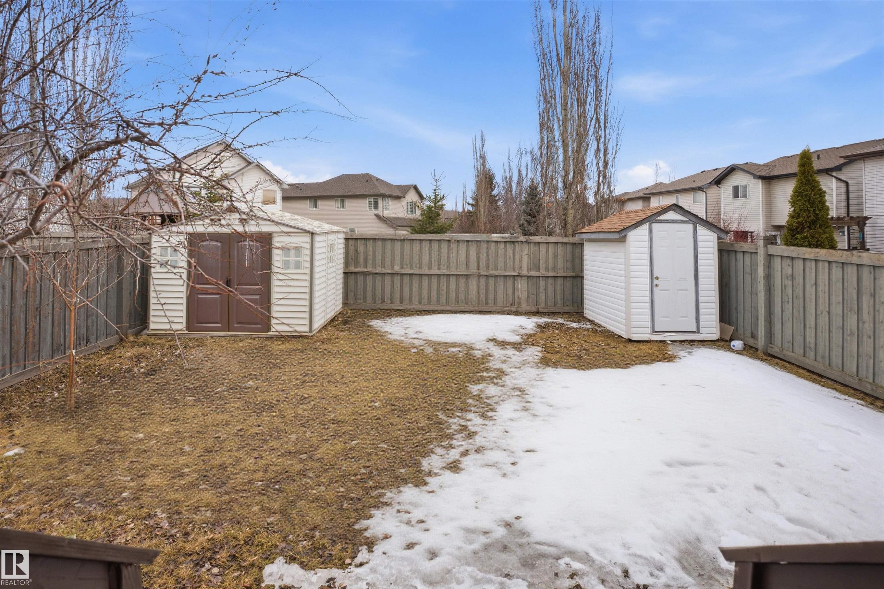 The yard features two storage sheds, a wooden fence, and mature trees - 4619 202 Street, Edmonton, AB - Outdoor