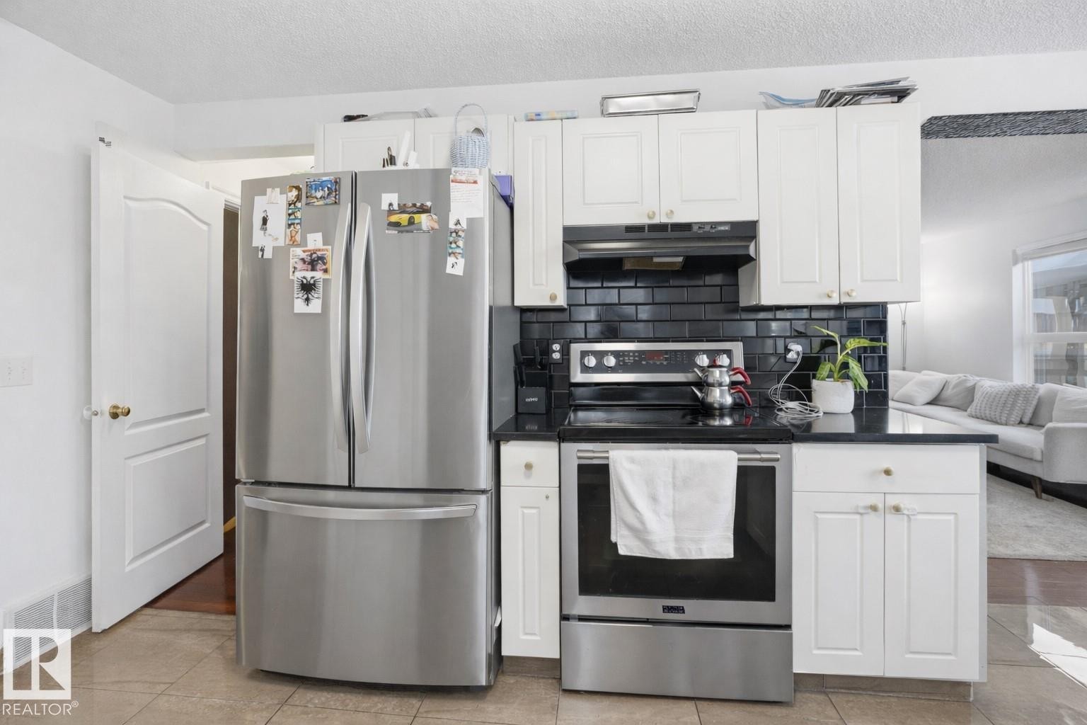 The kitchen features white cabinetry, a black subway tile backsplash, and stainless steel appliances including a refrigerator and range - 4619 202 Street, Edmonton, AB - Indoor Photo Showing Kitchen