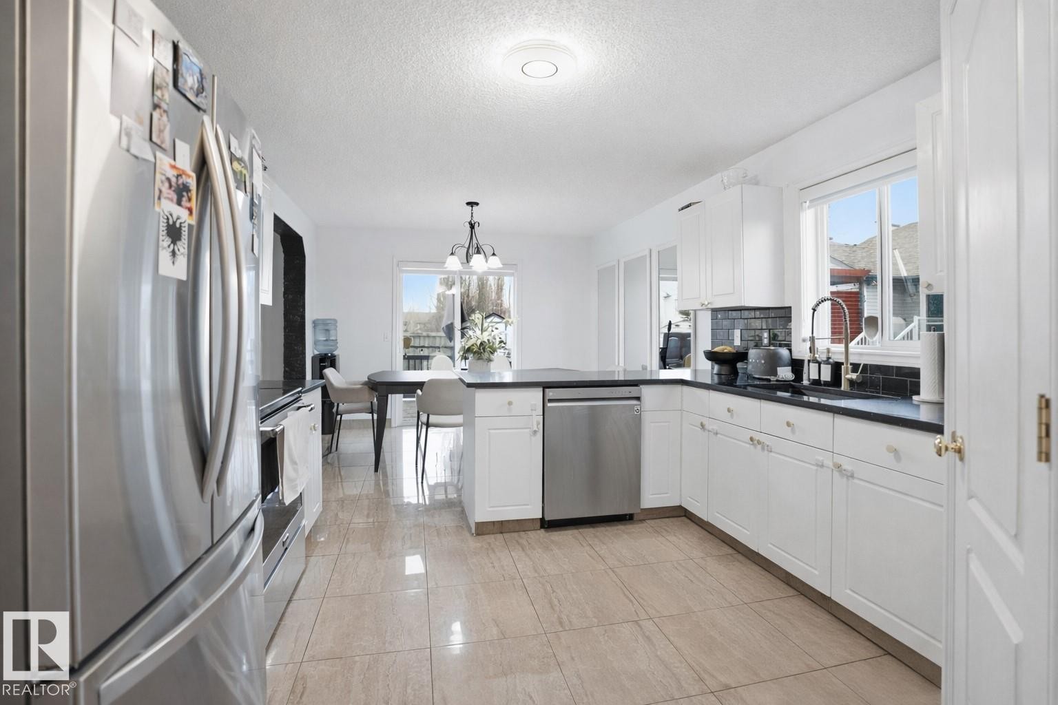 The kitchen features white cabinetry, dark countertops, stainless steel appliances, and a tile floor - 4619 202 Street, Edmonton, AB - Indoor Photo Showing Kitchen With Upgraded Kitchen