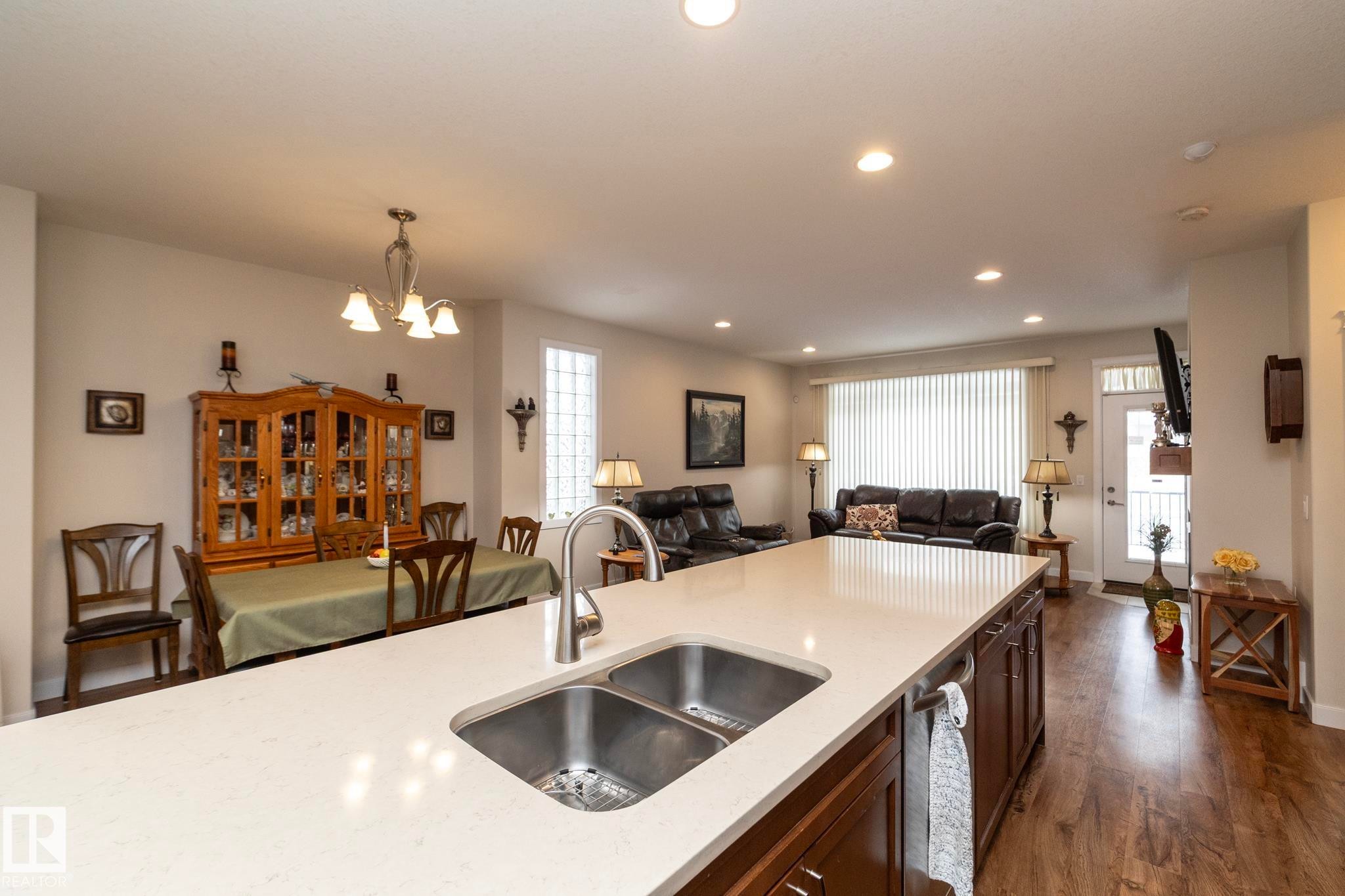 The property features a kitchen island with a double sink and ample countertop space, overlooking an open-concept living area - 307 Ravine Close, Devon, AB - Indoor Photo Showing Kitchen With Double Sink