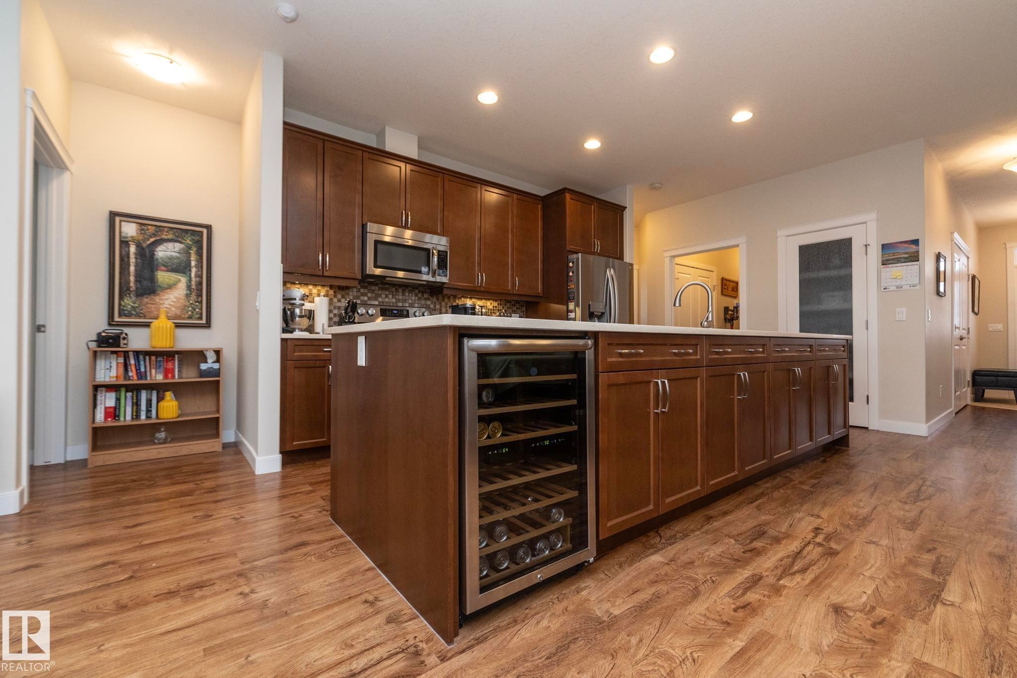 The kitchen features a large island with a built-in wine cooler, wood cabinetry, and stainless steel appliances - 307 Ravine Close, Devon, AB - Indoor Photo Showing Kitchen