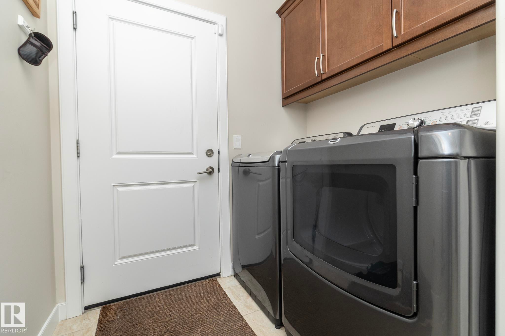 Laundry room featuring light-colored walls, wood-finish cabinetry, and a pair of dark-colored appliances - 307 Ravine Close, Devon, AB - Indoor Photo Showing Laundry Room
