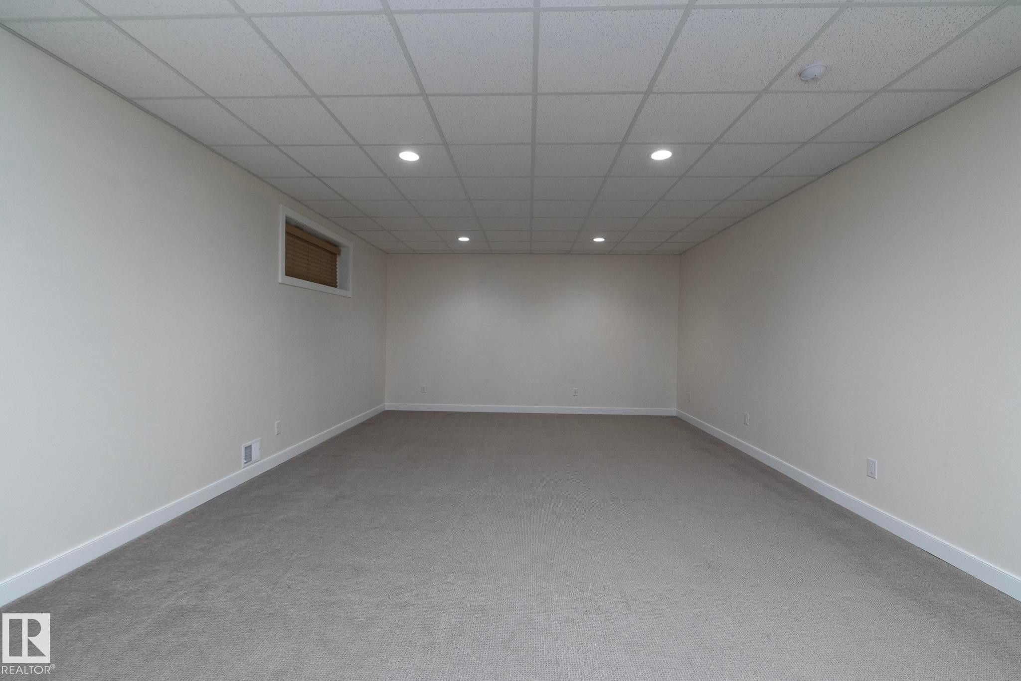 This spacious room features neutral-toned carpet flooring, white walls, and a dropped ceiling with recessed lighting - 307 Ravine Close, Devon, AB - Indoor Photo Showing Other Room