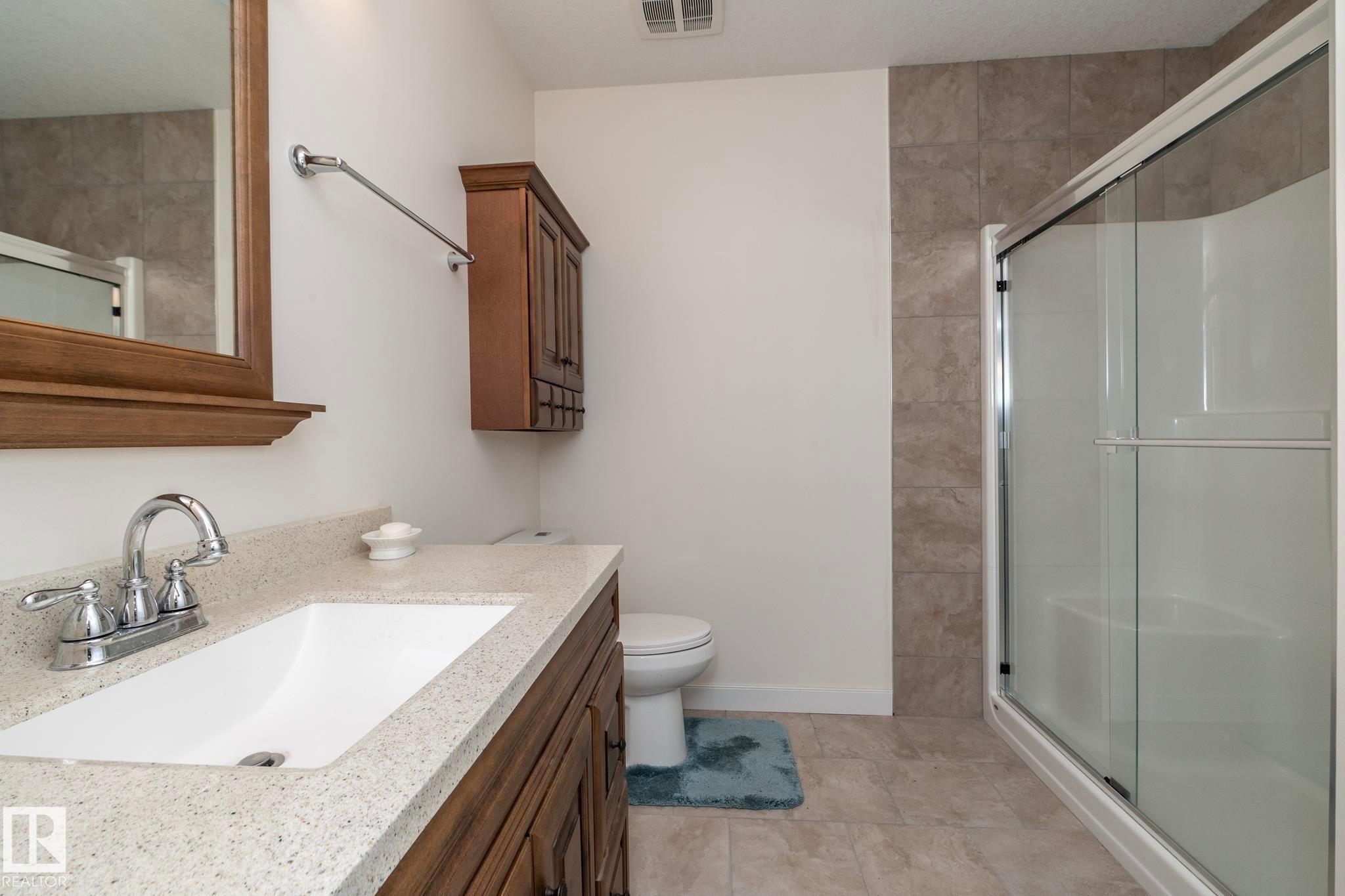 Bathroom featuring a vanity with a light-colored countertop and wooden cabinetry, a shower with a sliding glass door, and tiled flooring - 307 Ravine Close, Devon, AB - Indoor Photo Showing Bathroom