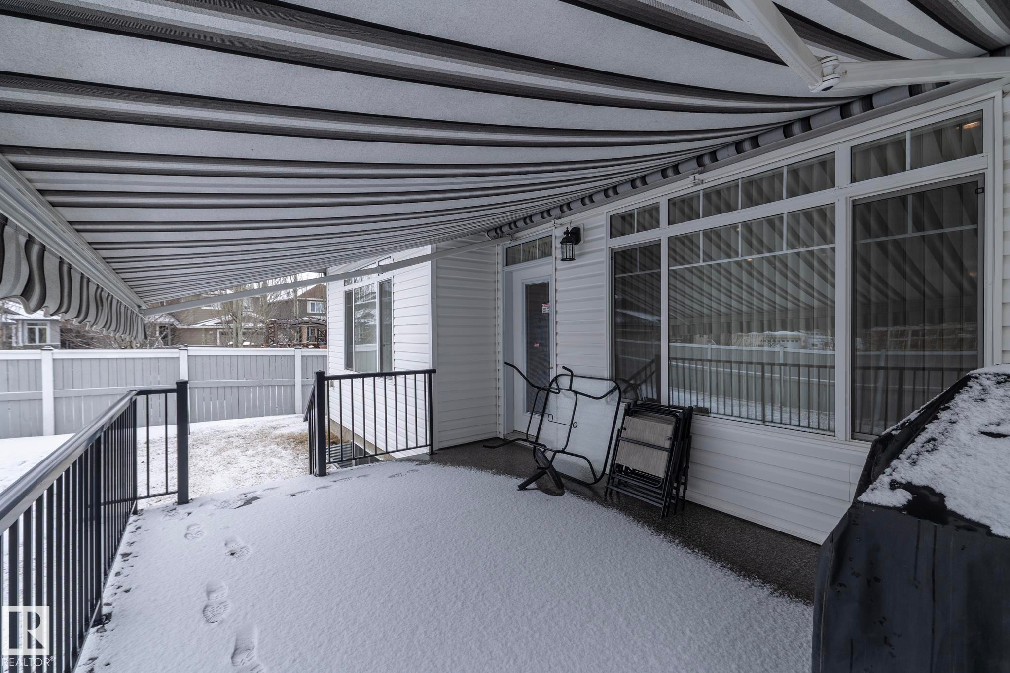 This property features a covered patio with a striped awning, white siding, and a large window - 307 Ravine Close, Devon, AB - Outdoor With Exterior