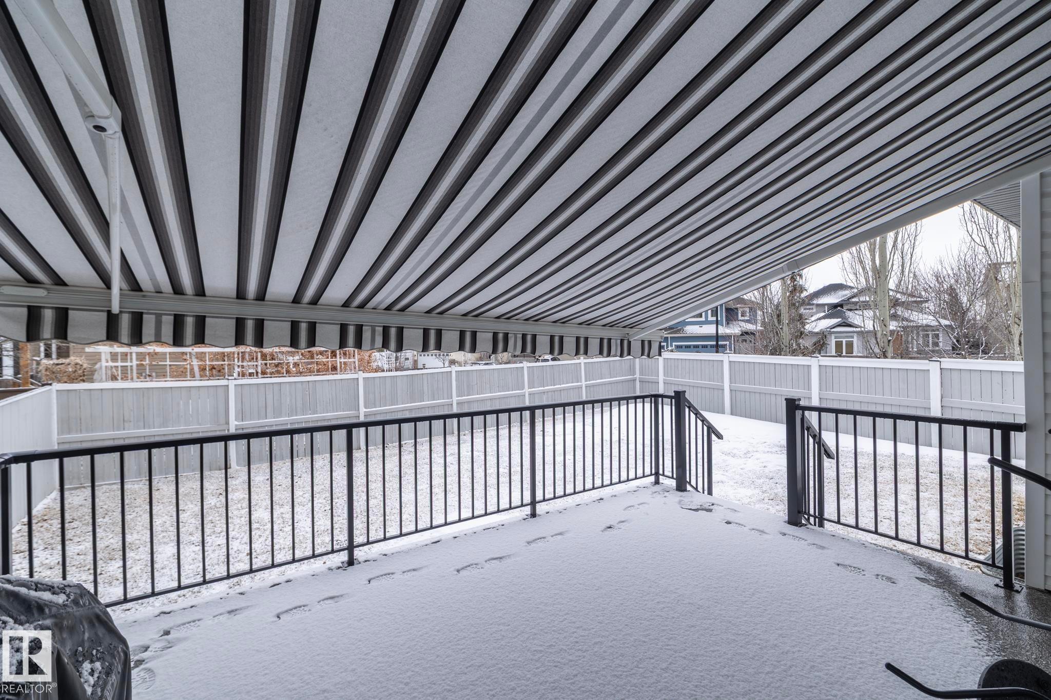 The property features a patio with a striped awning and black metal railings, overlooking a fenced yard - 307 Ravine Close, Devon, AB - Outdoor
