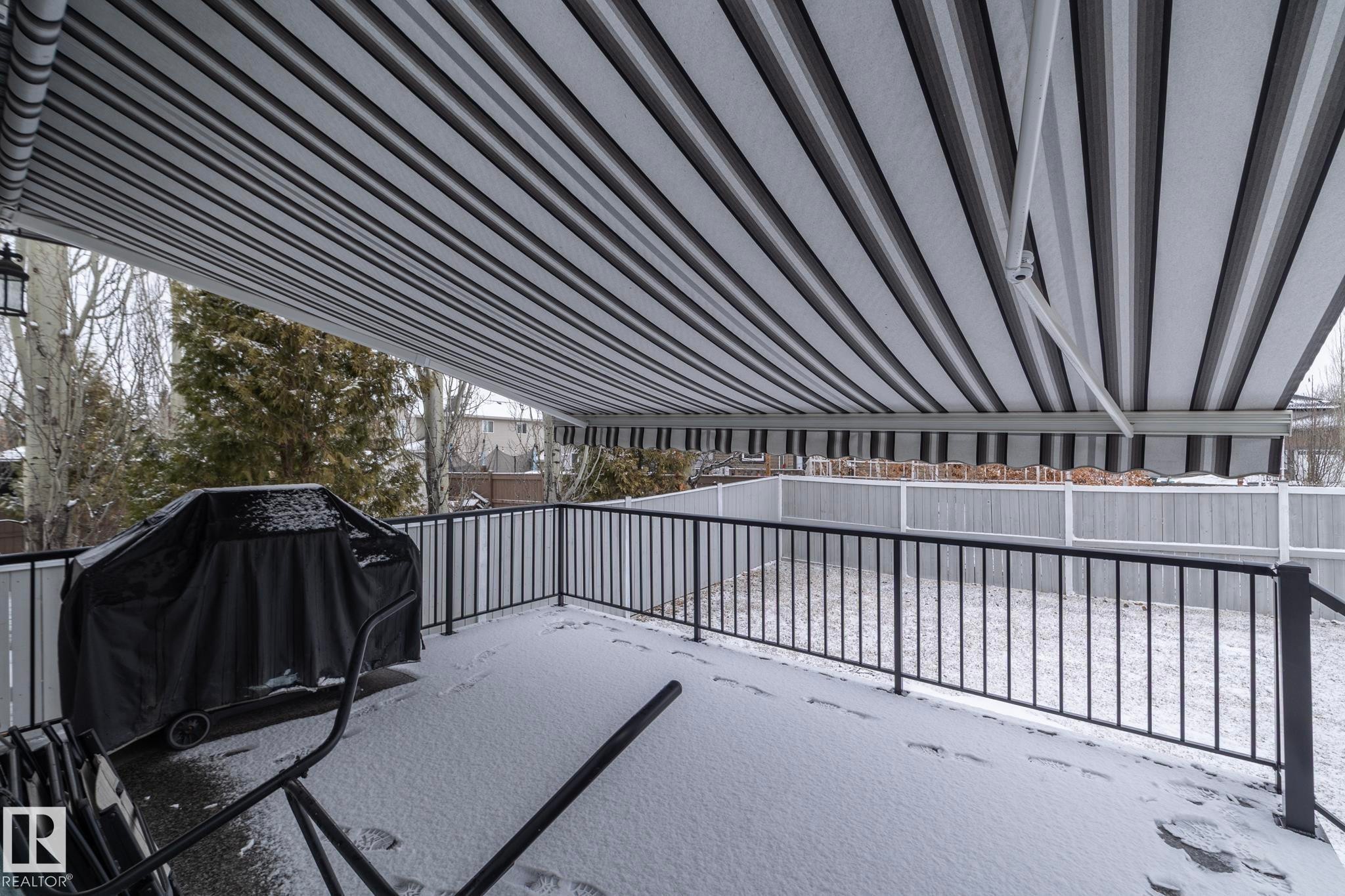 Outdoor deck space with a striped retractable awning, black metal railing, and privacy fencing - 307 Ravine Close, Devon, AB - Outdoor With Exterior