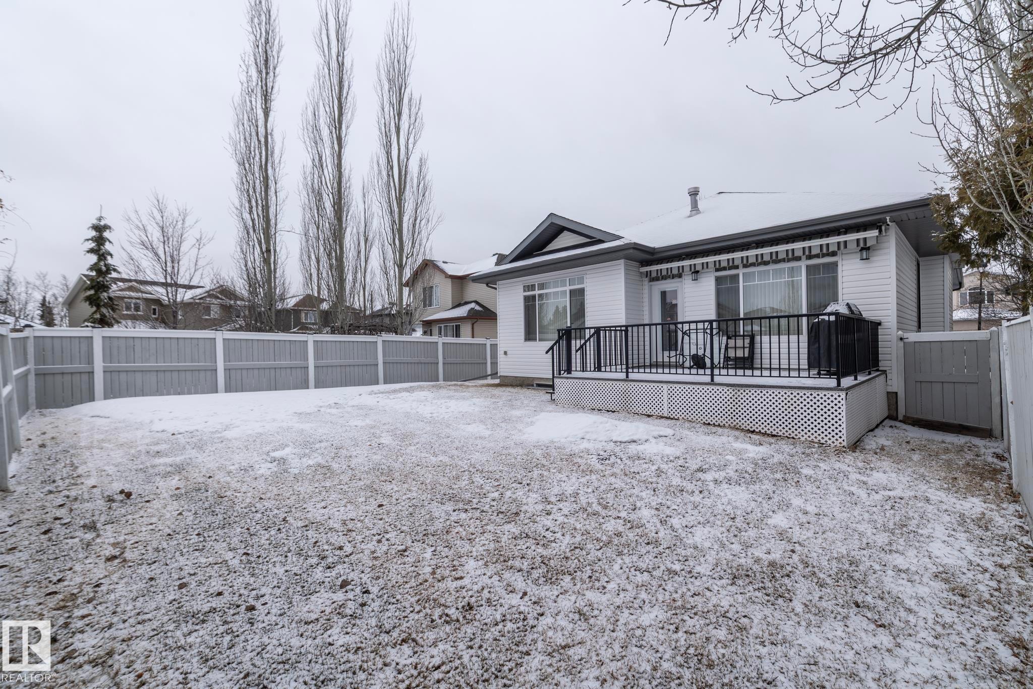 The property features a spacious yard with a deck, complete with a dark metal railing and white lattice skirting - 307 Ravine Close, Devon, AB - Outdoor With Deck Patio Veranda