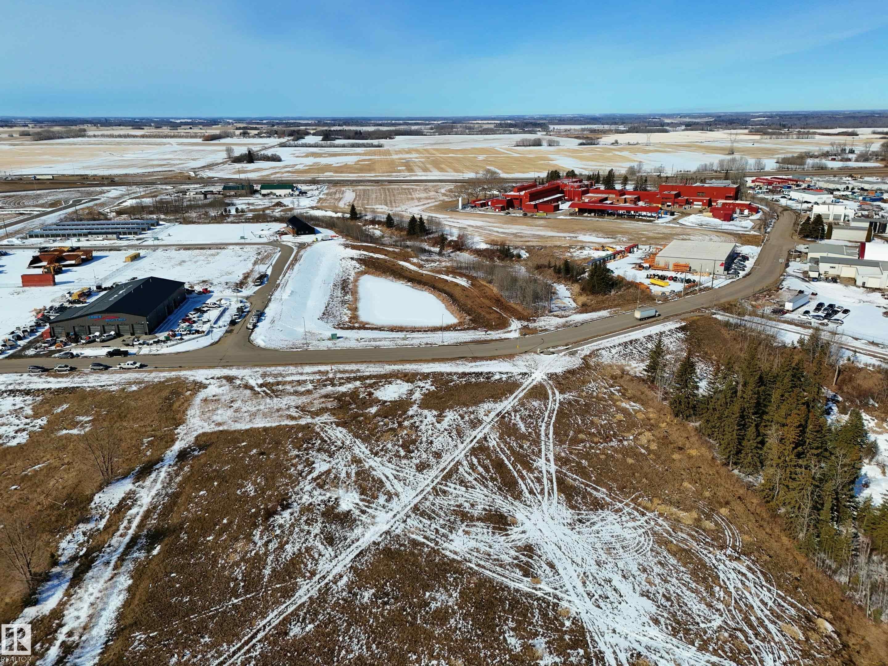 Aerial view of the property and its surrounding area, featuring cleared land, a paved road, and distant buildings - 307 Ravine Close, Devon, AB - Outdoor With View