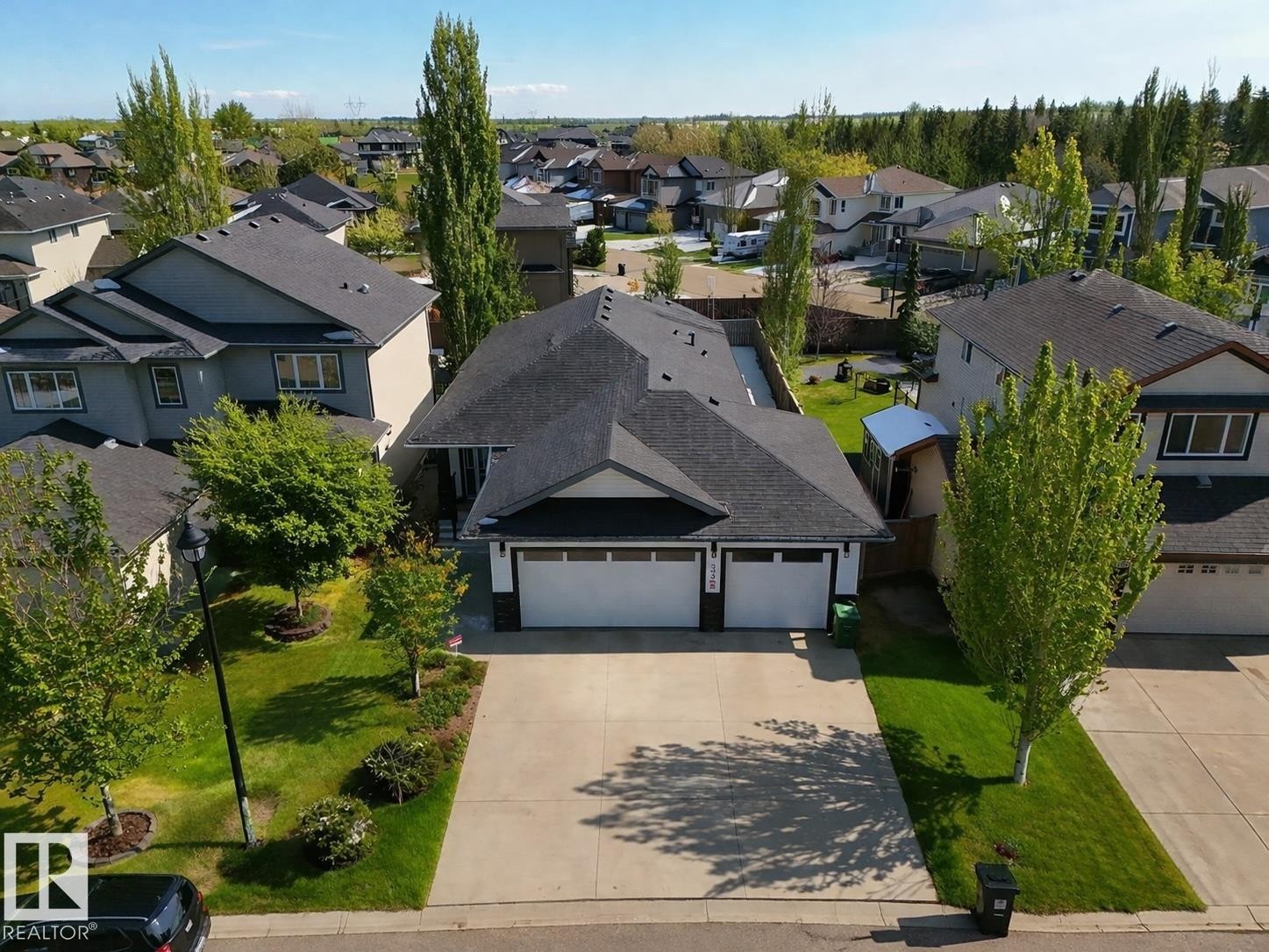 The property features a dark shingle roof, a light-colored driveway, and a well-maintained lawn with mature trees and shrubs - 307 Ravine Close, Devon, AB - Outdoor