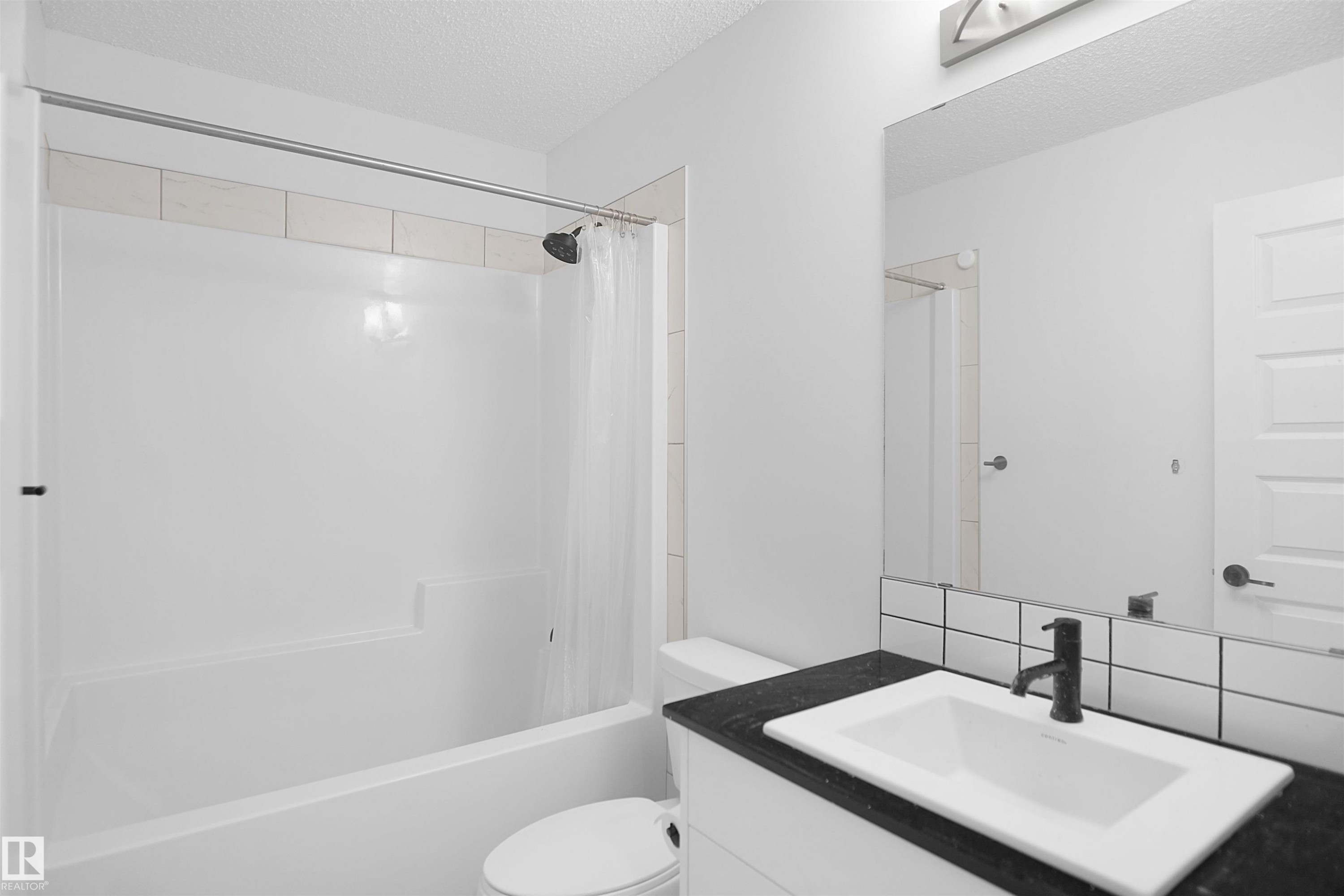 Bathroom featuring a white bathtub with a shower head, a white vanity with a dark countertop and a rectangular sink, and a large wall-mounted mirror - Edmonton, AB - Indoor Photo Showing Bathroom
