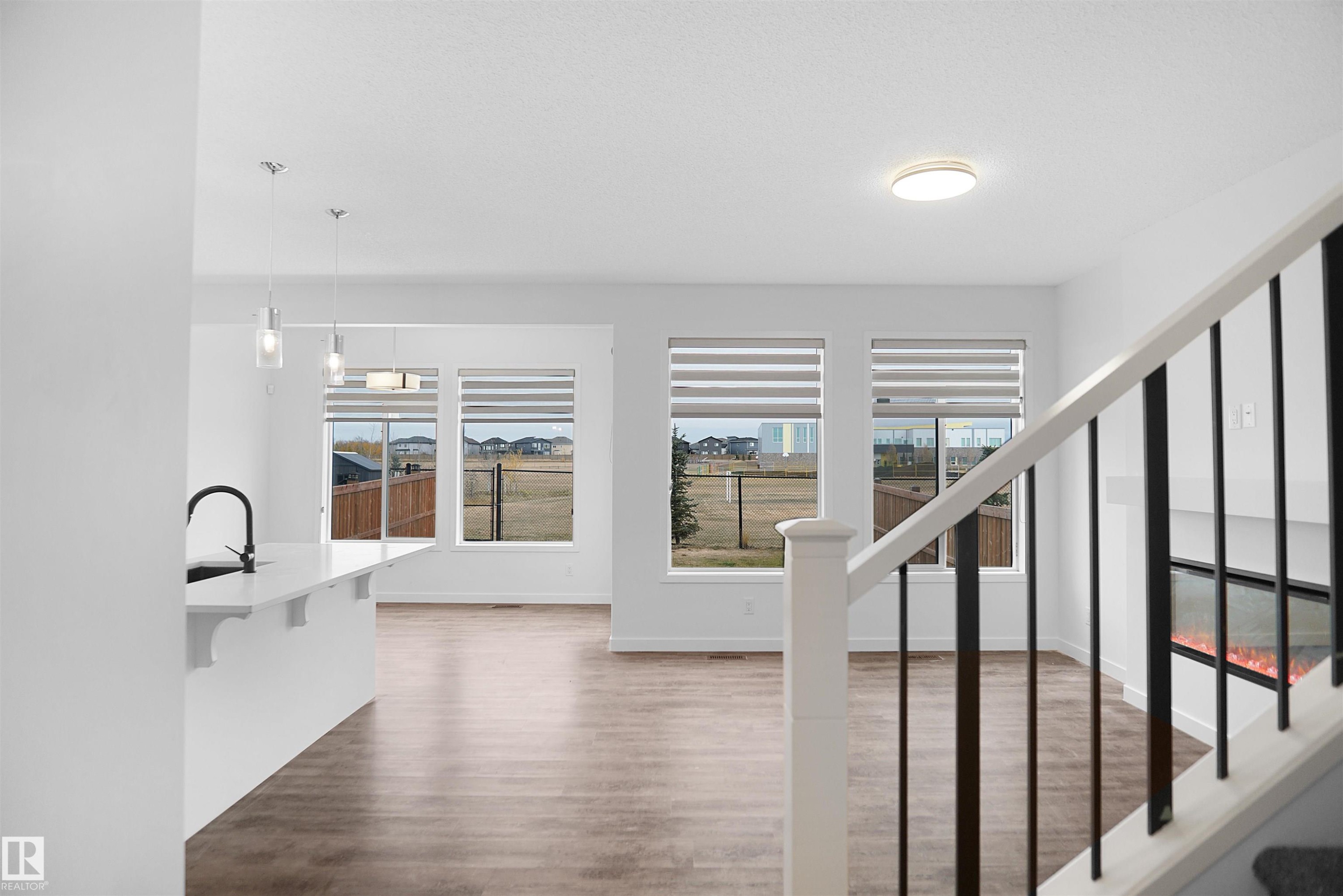 Open concept living area featuring hardwood flooring, a white kitchen island with a dark faucet, and large windows with blinds - Edmonton, AB - Indoor Photo Showing Other Room