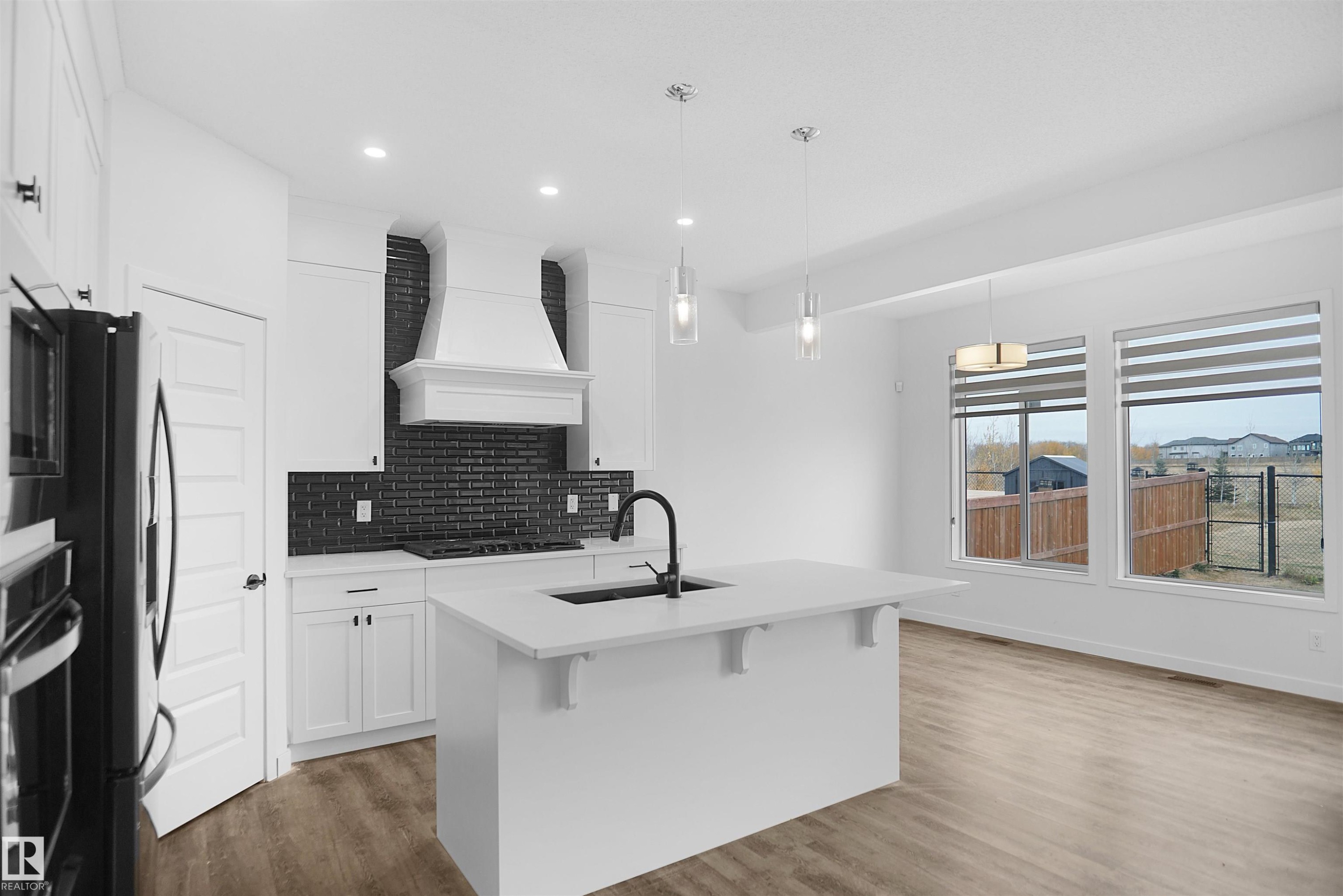 The kitchen features white cabinetry, a black subway tile backsplash, and a large island with a sink and modern pendant lighting - Edmonton, AB - Indoor Photo Showing Kitchen With Upgraded Kitchen