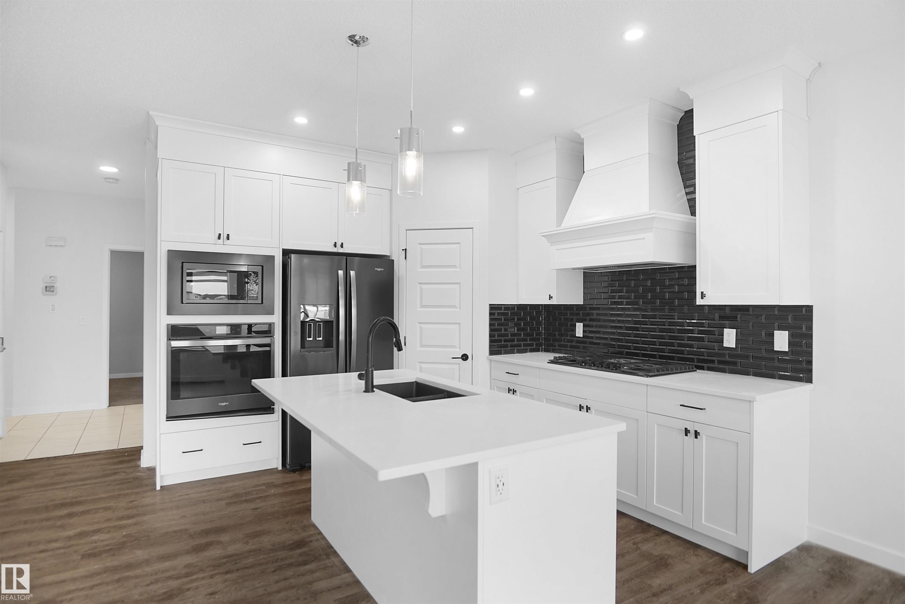 The kitchen features white cabinetry, a large island with a sink, a black subway tile backsplash, and dark stainless steel appliances - Edmonton, AB - Indoor Photo Showing Kitchen With Upgraded Kitchen