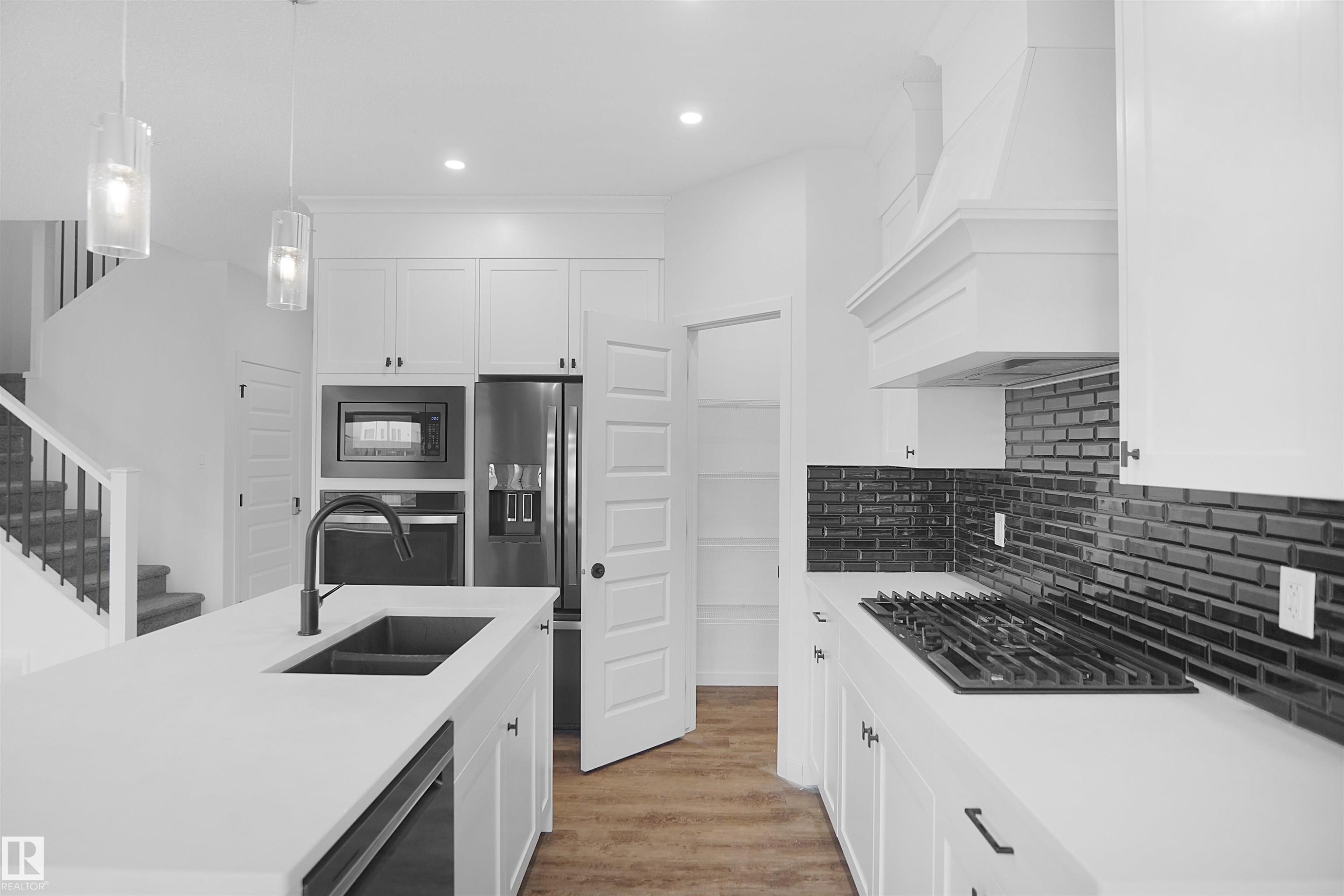The kitchen features white cabinetry, a dark subway tile backsplash, and a large island with an integrated sink - Edmonton, AB - Indoor Photo Showing Kitchen With Double Sink With Upgraded Kitchen