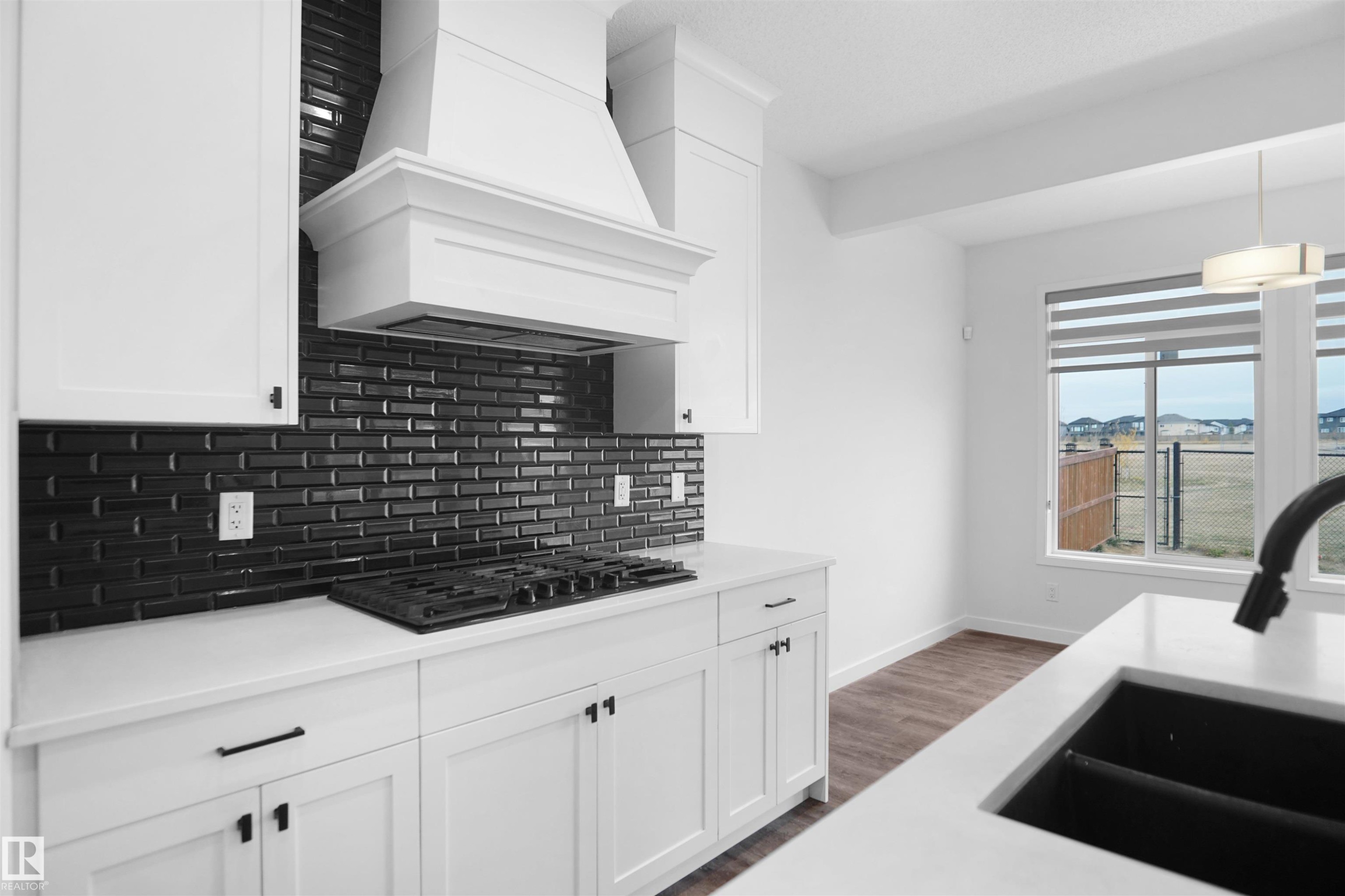 The kitchen features white cabinetry, a dark subway tile backsplash, a built-in range, and a large window providing views of the open landscape - Edmonton, AB - Indoor Photo Showing Kitchen With Upgraded Kitchen