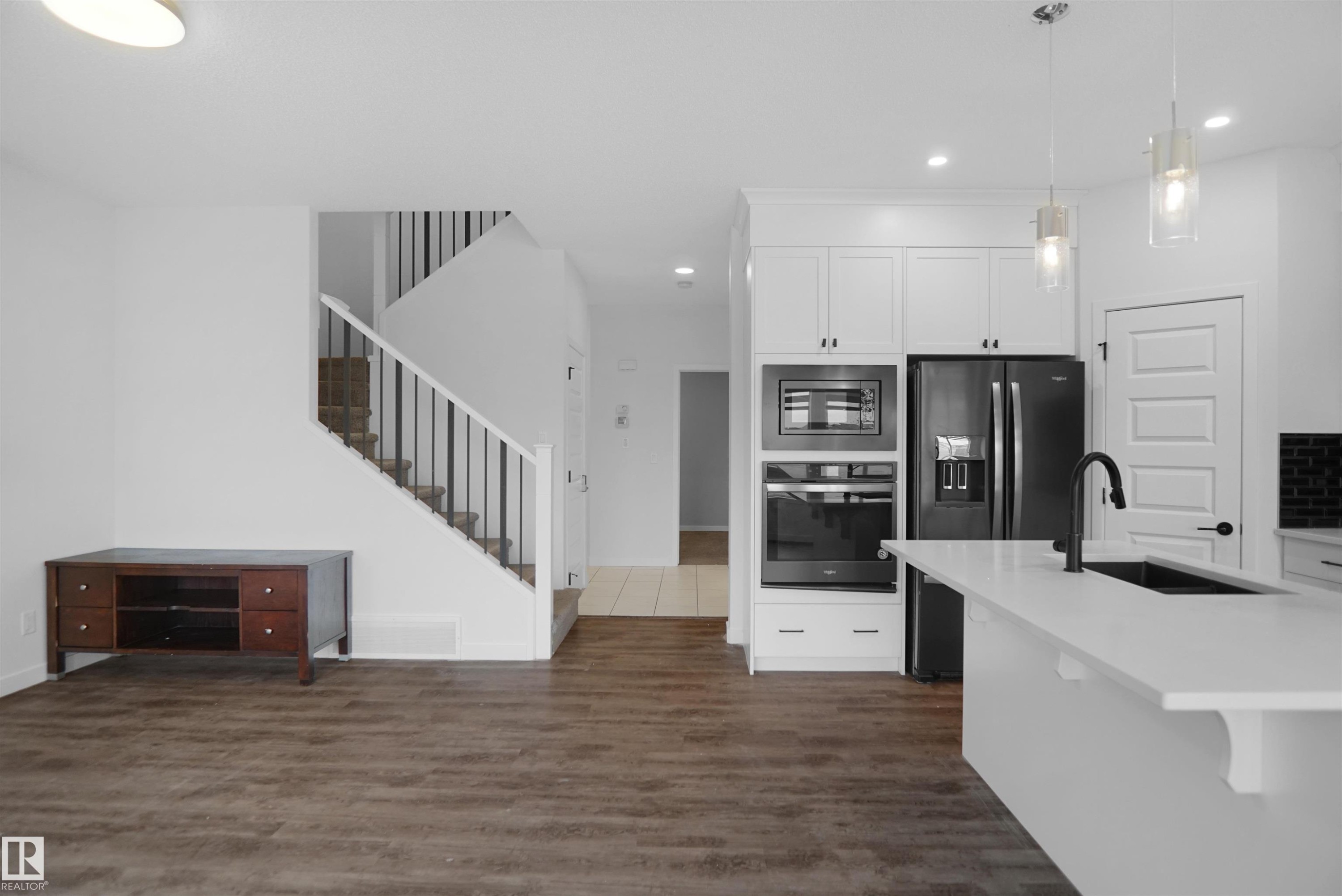 Open concept living area featuring dark wood-style flooring and a staircase with white risers and handrails - Edmonton, AB - Indoor Photo Showing Kitchen With Upgraded Kitchen