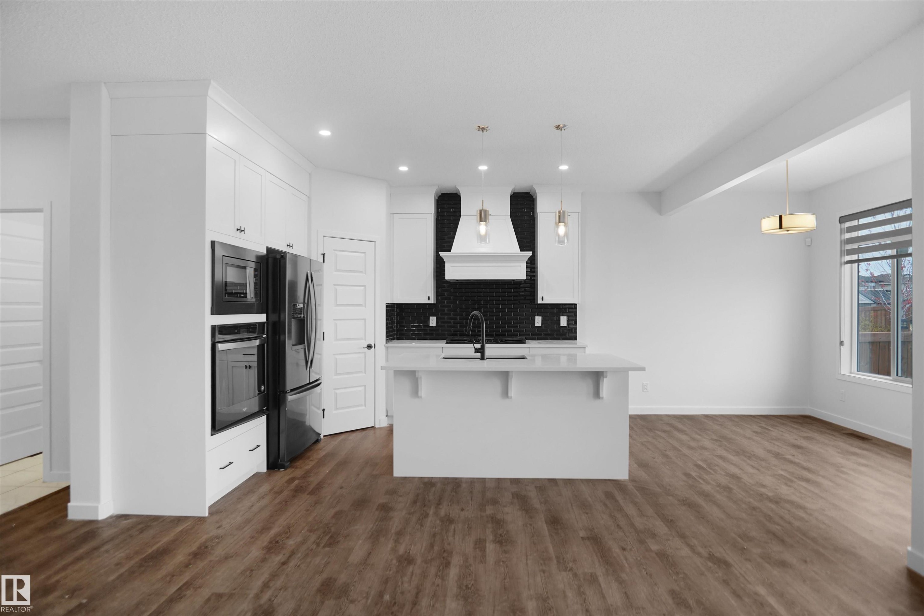 The kitchen features white cabinetry, a kitchen island with a sink, a dark tiled backsplash, and recessed lighting - Edmonton, AB - Indoor Photo Showing Kitchen