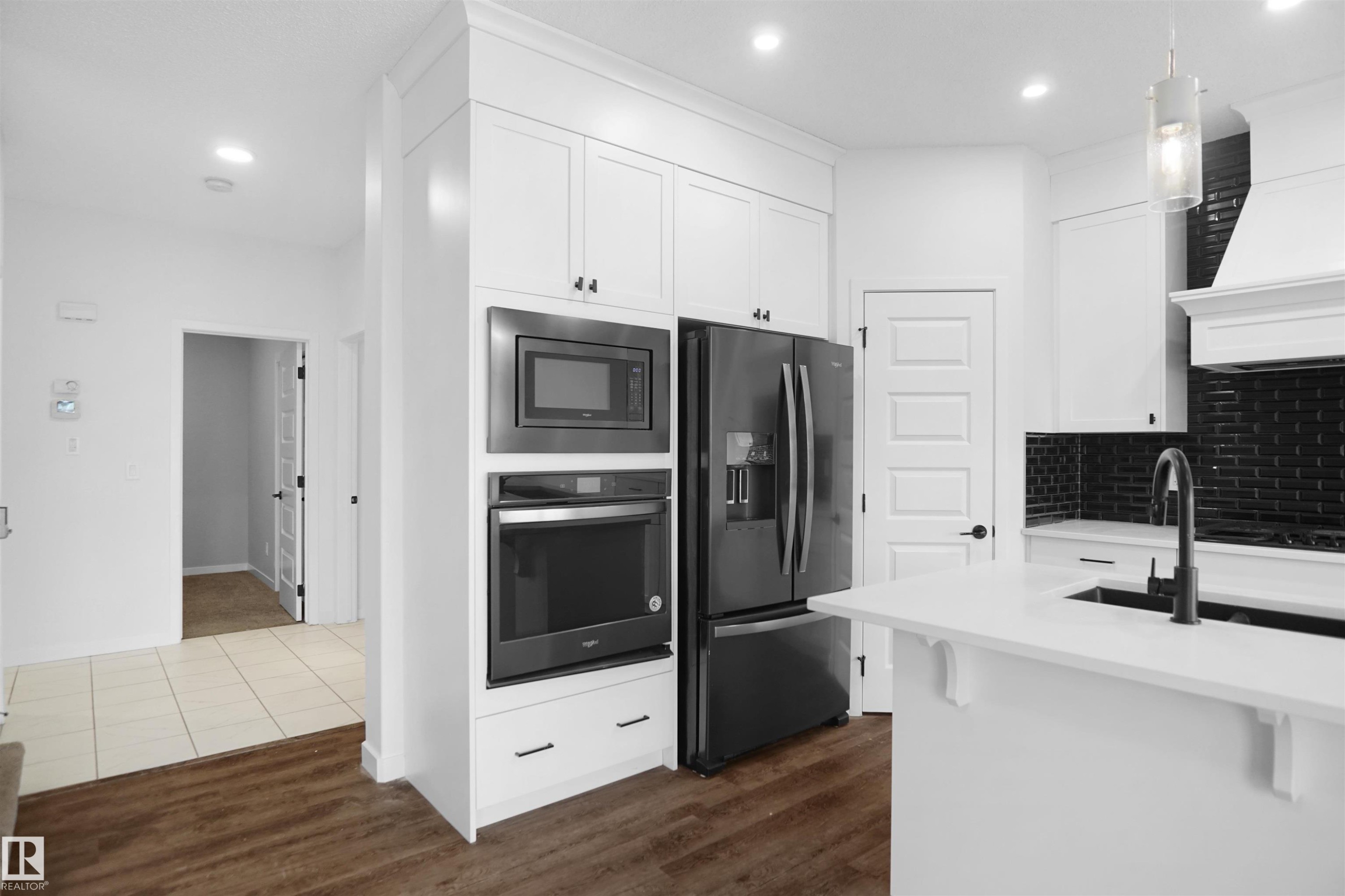 The property offers a modern kitchen featuring white cabinetry, dark stainless steel appliances, a kitchen island with a sink and a black tiled backsplash - Edmonton, AB - Indoor Photo Showing Kitchen With Upgraded Kitchen