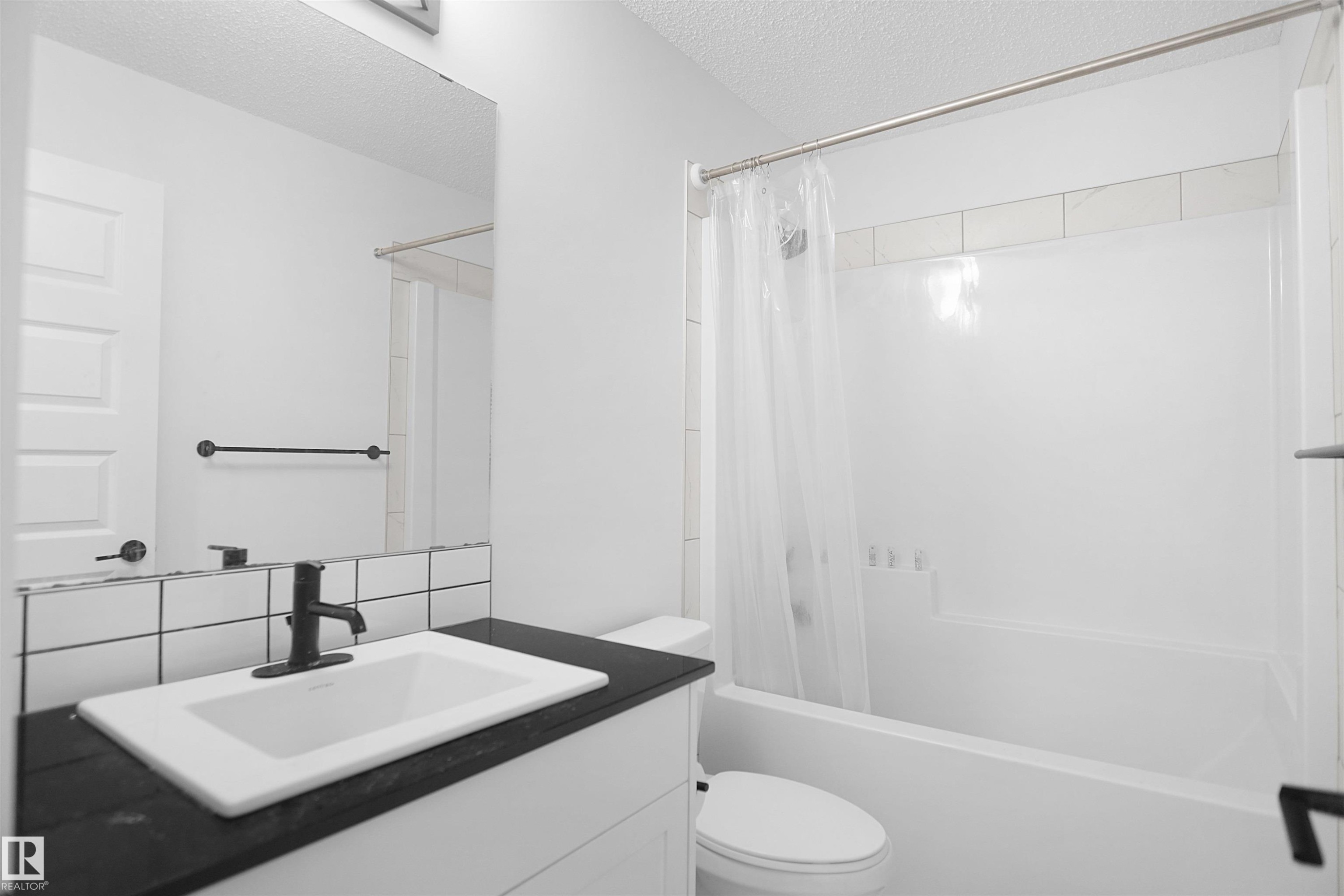 Bathroom featuring a vanity with a dark countertop and white sink, a mirror, and a bathtub with a shower - Edmonton, AB - Indoor Photo Showing Bathroom