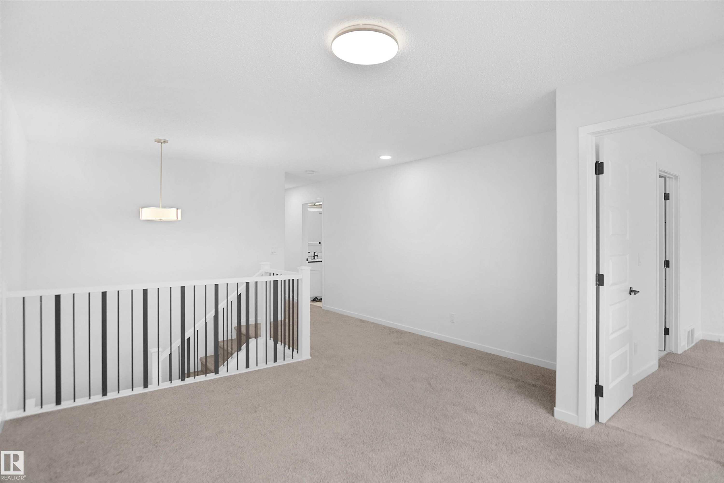 The property features a spacious landing with neutral carpeting, a staircase with white and black railings, and a modern ceiling light fixture - Edmonton, AB - Indoor Photo Showing Other Room