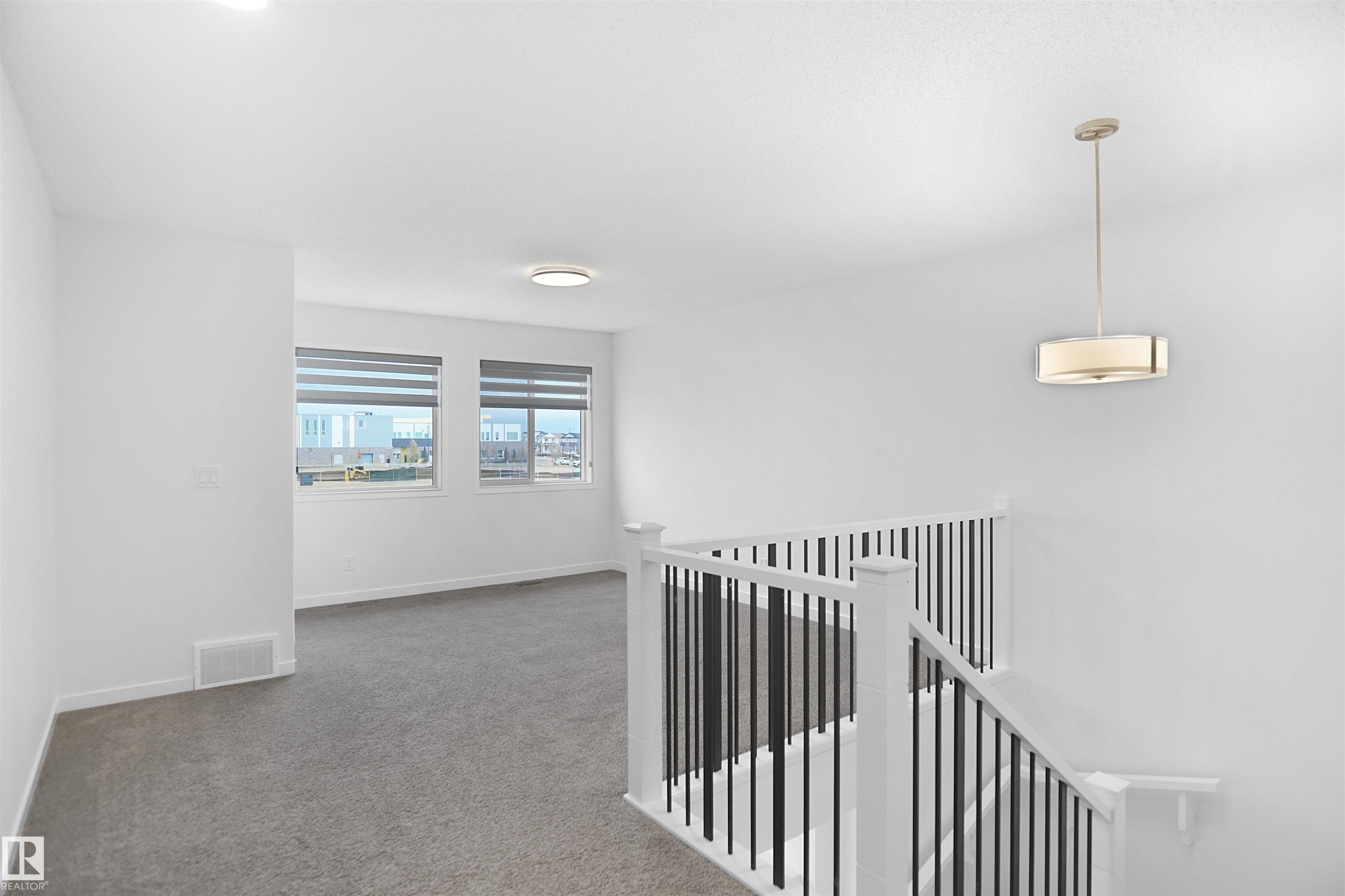 Bright, open area featuring neutral carpeting, two windows with blinds, and white walls - Edmonton, AB - Indoor Photo Showing Other Room