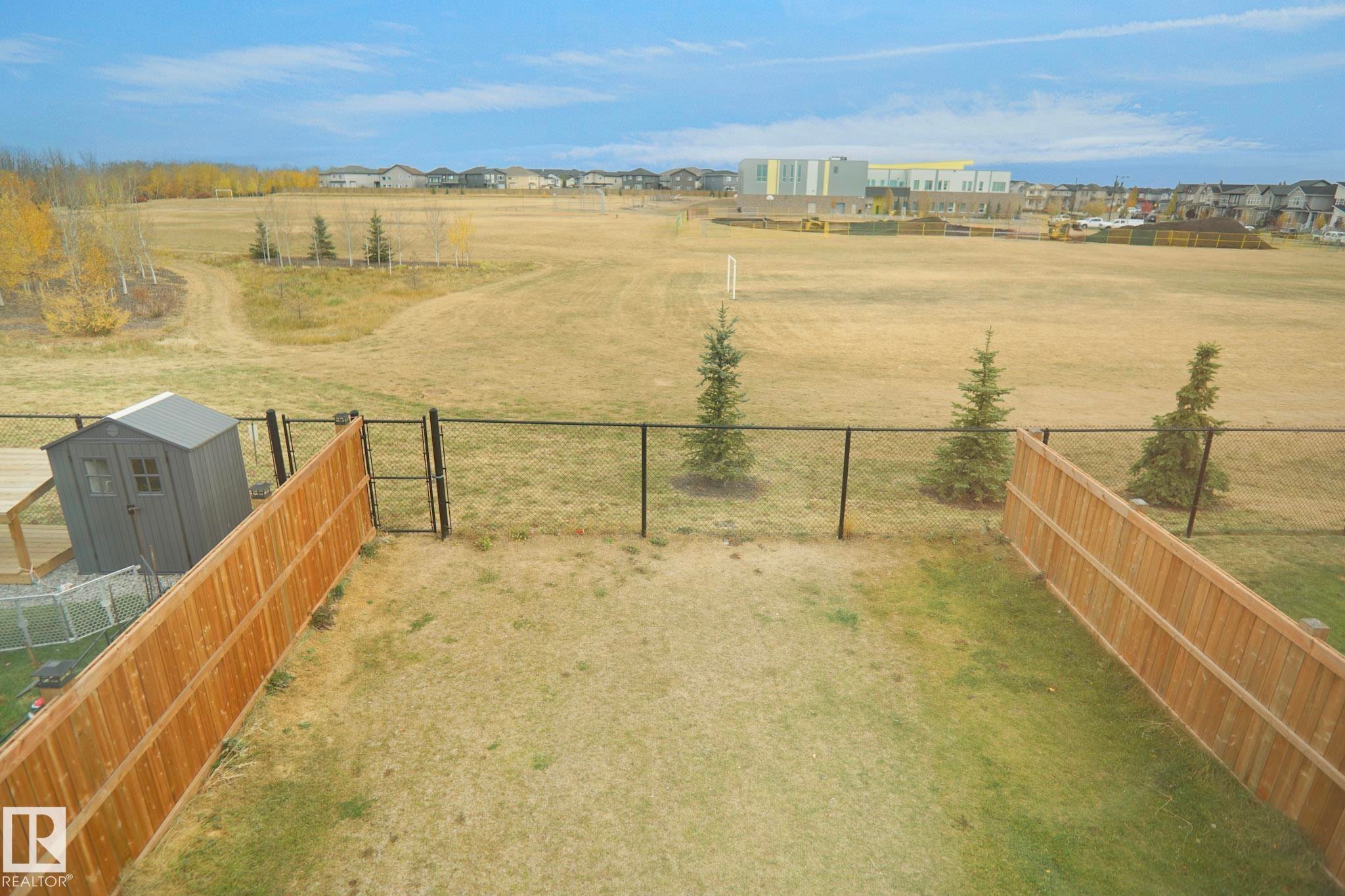 The property features a fenced yard with a gate, a storage shed, and a view of an expansive open field with trees - Edmonton, AB - Outdoor With View