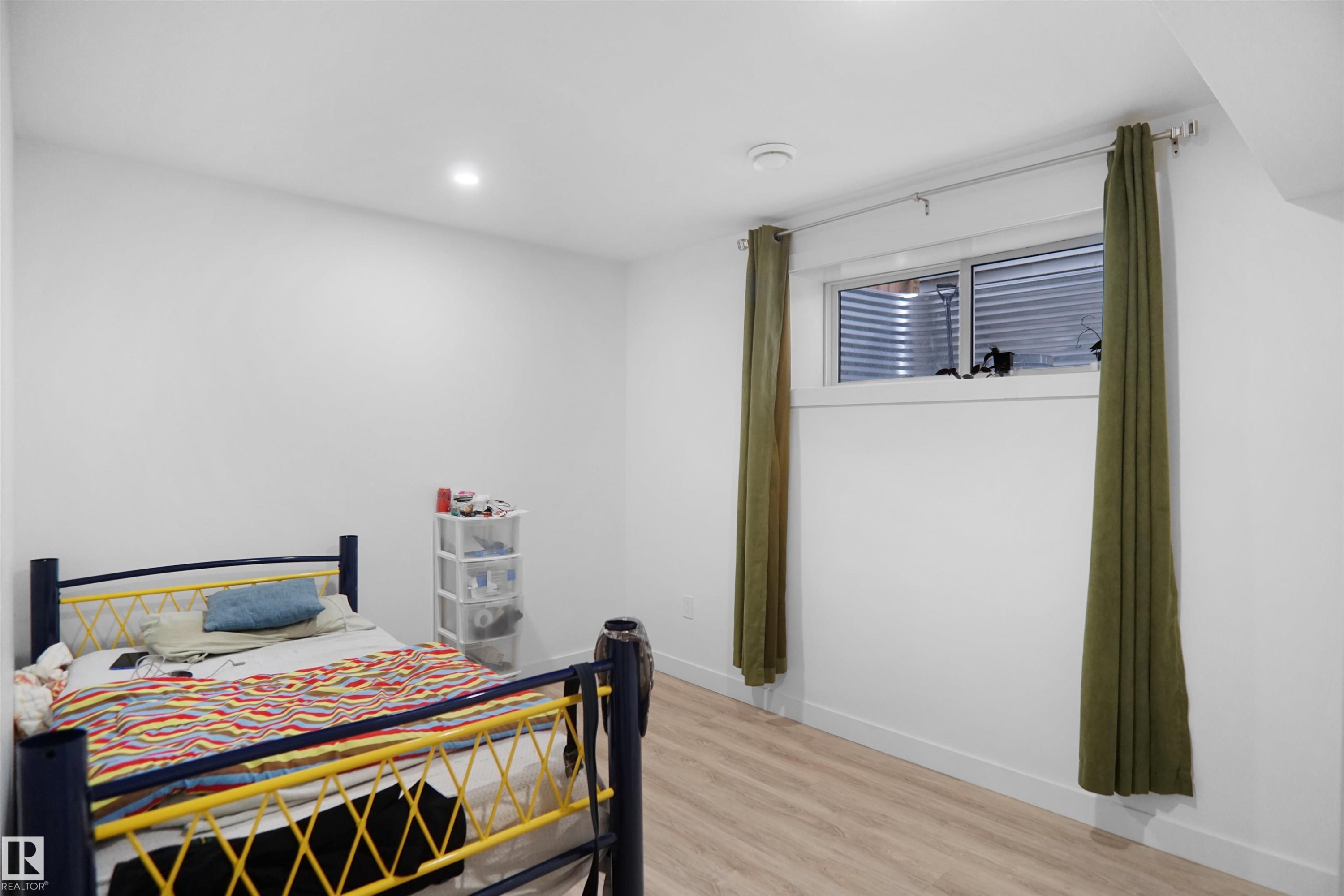 This inviting room features light-colored flooring, white walls, and a window with green drapes - Edmonton, AB - Indoor Photo Showing Bedroom