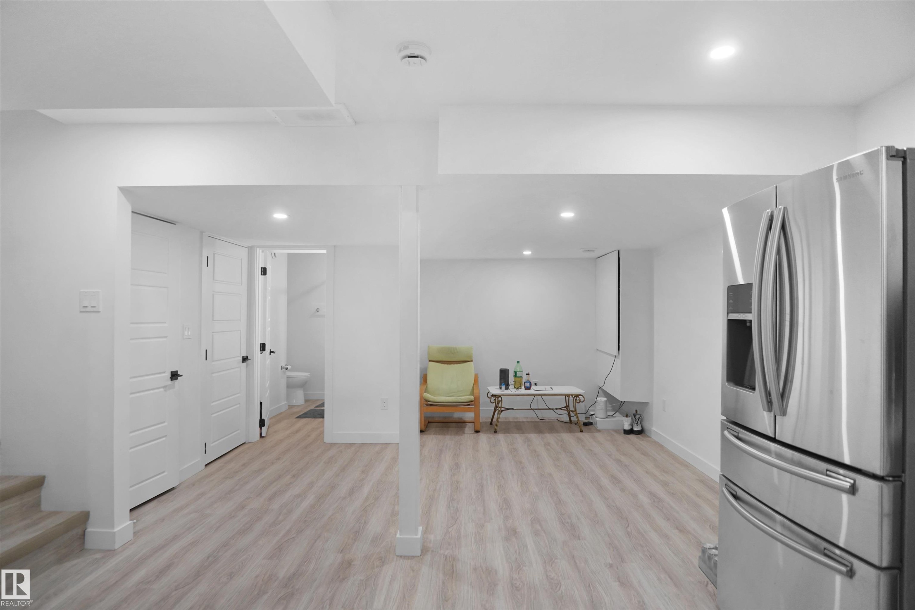 This open space features light-toned flooring, recessed lighting, and a stainless steel refrigerator - Edmonton, AB - Indoor Photo Showing Other Room