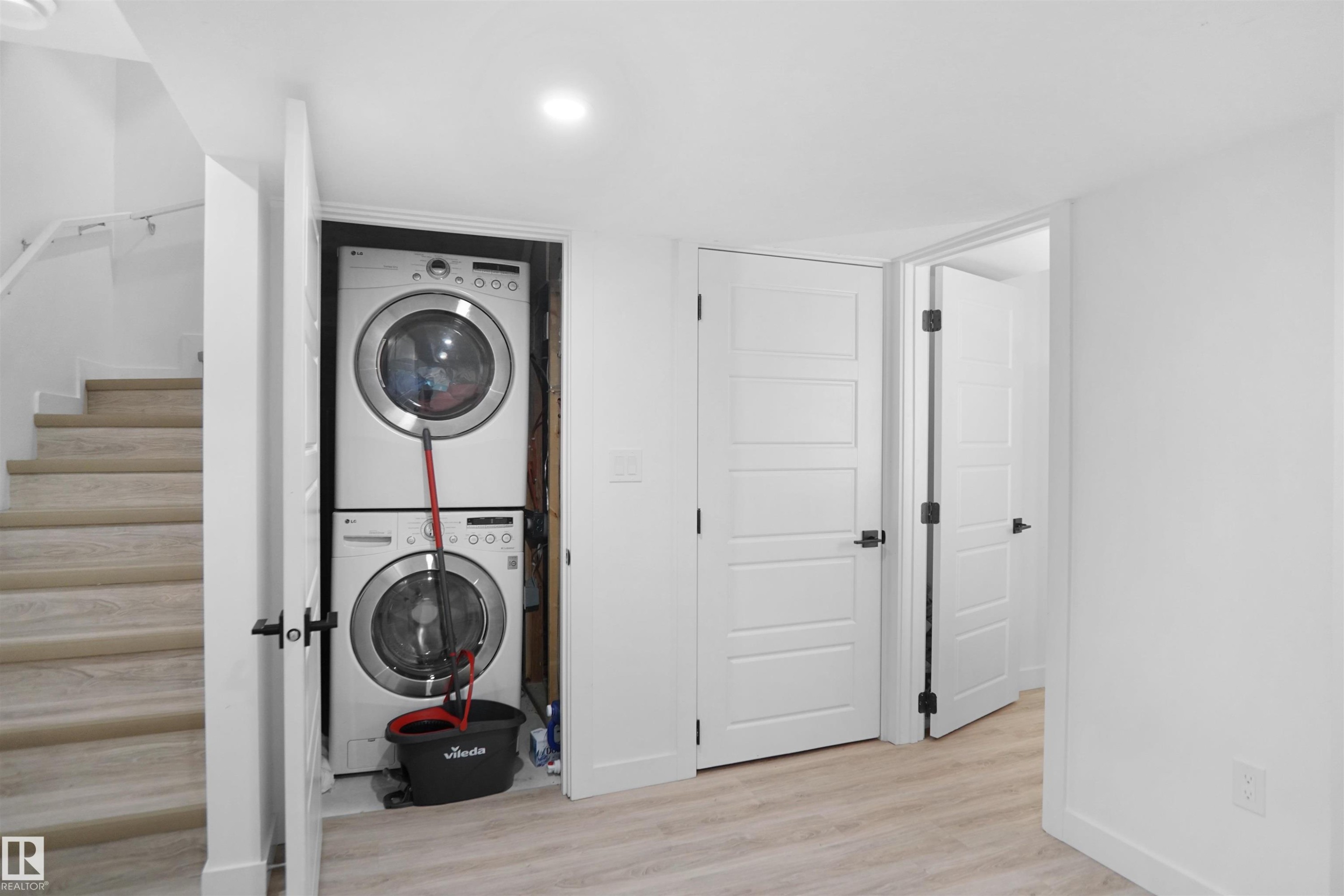 The property features a dedicated laundry area with a stacked washer and dryer, light-toned flooring, and white walls - Edmonton, AB - Indoor Photo Showing Laundry Room