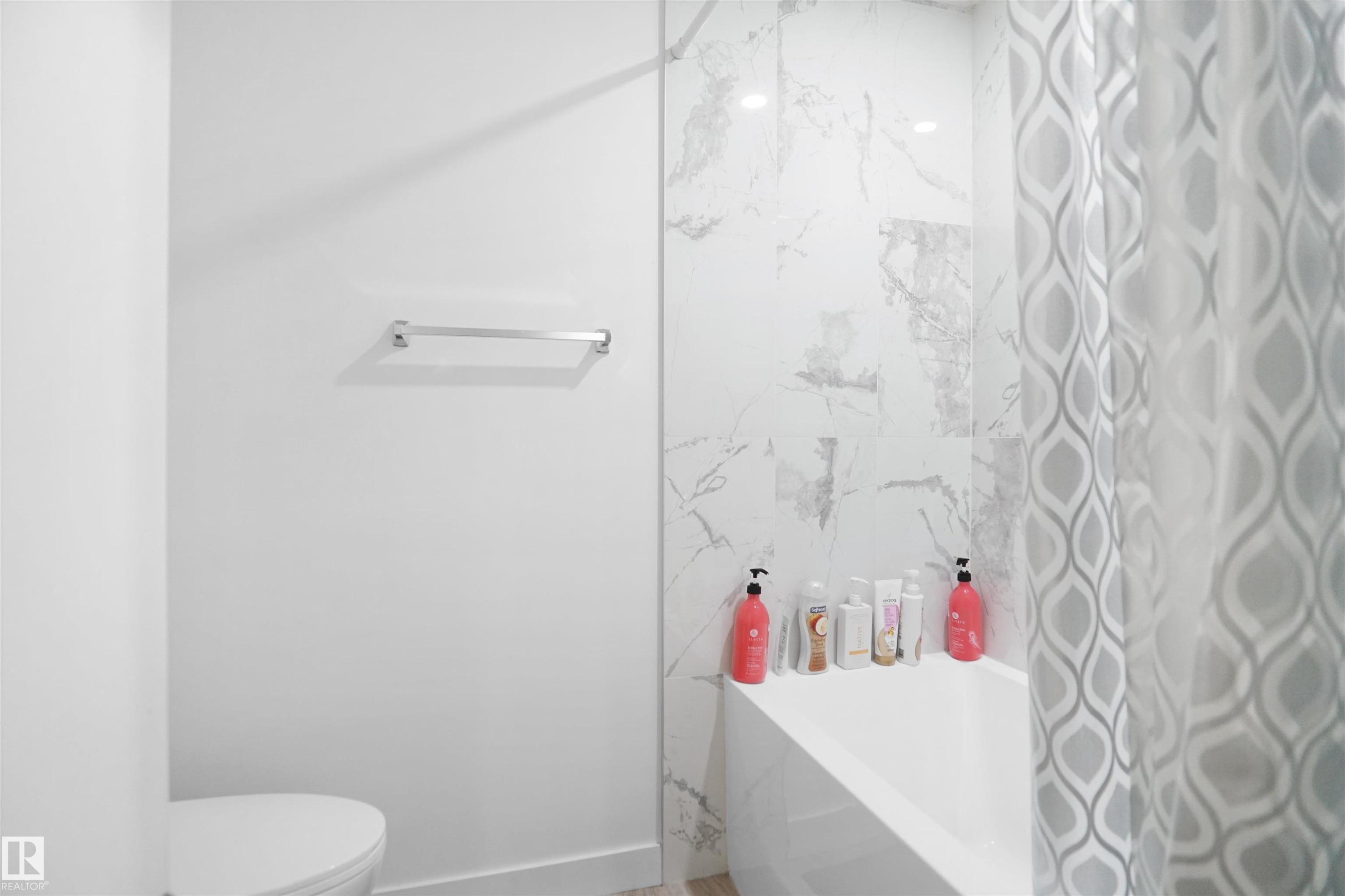 Bathroom featuring a white bathtub, a shower curtain with a geometric pattern, a towel bar, and white wall tiles with a grey marble-like pattern - Edmonton, AB - Indoor Photo Showing Bathroom