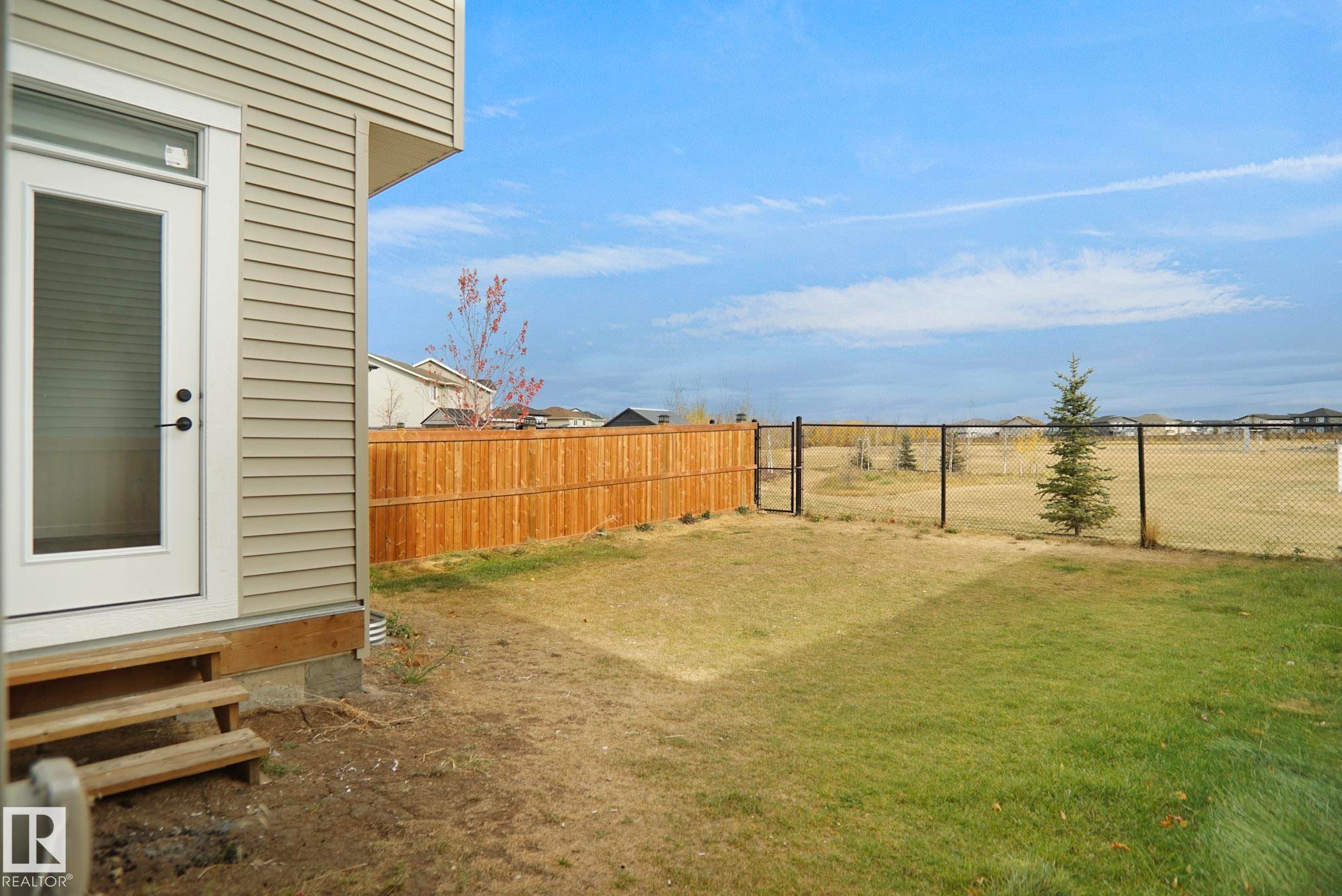 The property features a private backyard with a wooden fence and a chain link fence, offering an expansive view of the surrounding open space - Edmonton, AB - Outdoor