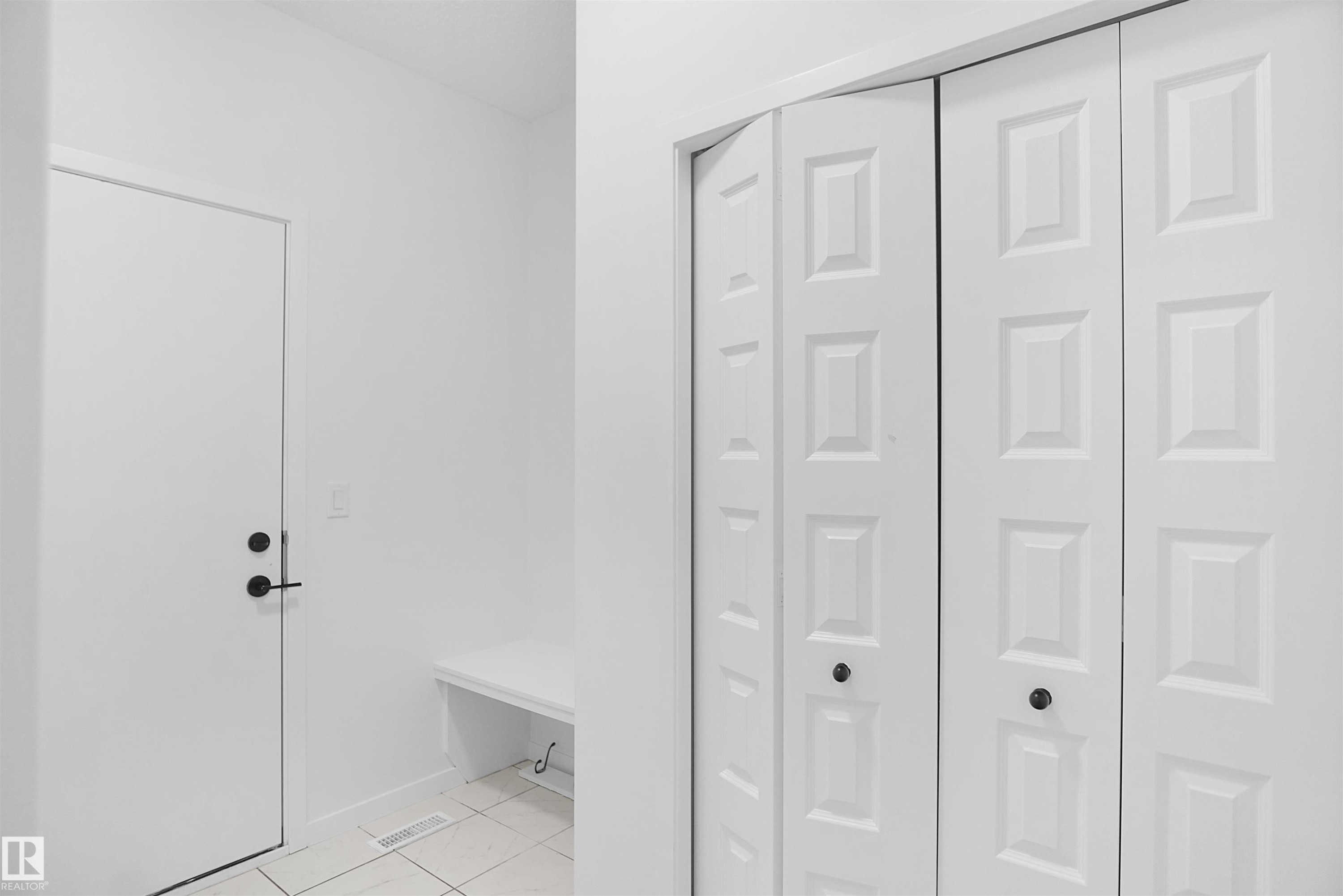 This entryway features a white door with black hardware, a built-in white bench, and bifold closet doors - Edmonton, AB - Indoor Photo Showing Other Room