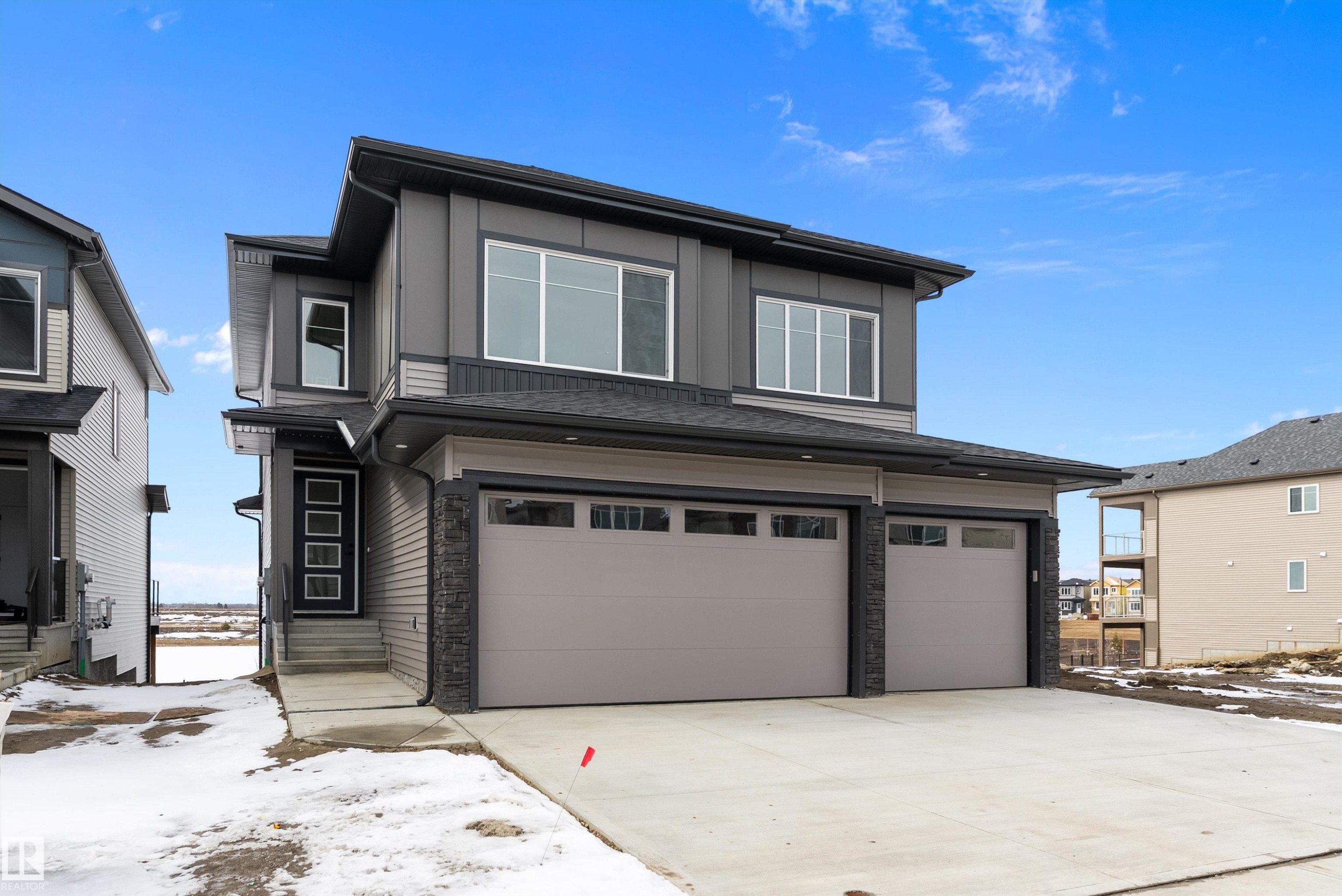 Modern property exterior featuring a dark grey facade with light grey accents, a two-car garage with panelled doors, and a concrete driveway - 219 Crystal Creek Dr, Leduc, AB - Outdoor