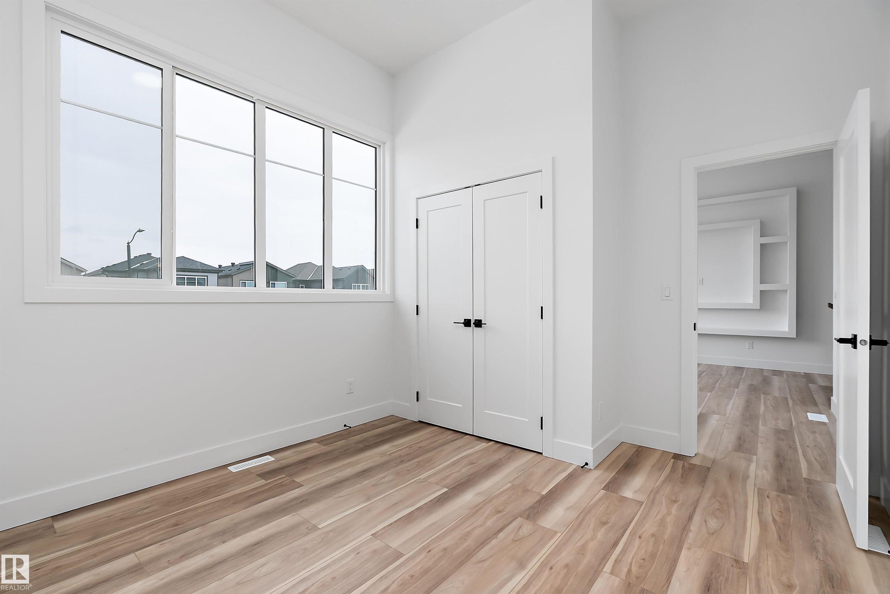 This room features light-toned hardwood flooring, a large window providing natural light, and two white doors with dark hardware - 219 Crystal Creek Dr, Leduc, AB - Indoor Photo Showing Other Room