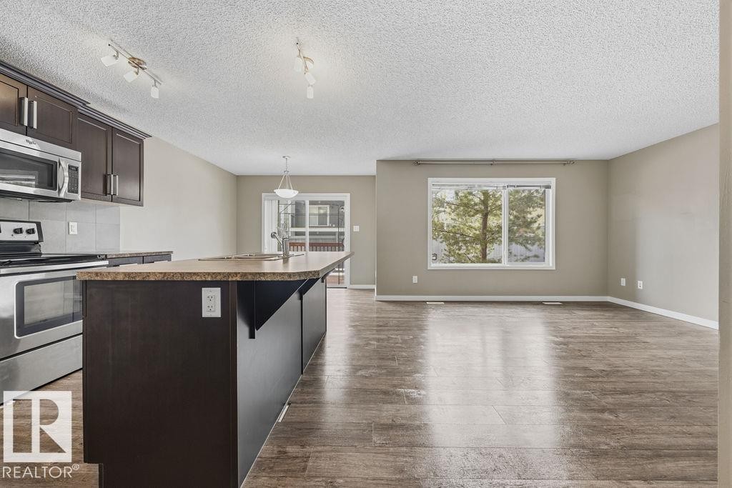 This kitchen features dark wood cabinetry, stainless steel appliances, and a central island with a granite countertop - 7873 170A Avenue, Edmonton, AB - Indoor Photo Showing Kitchen With Upgraded Kitchen