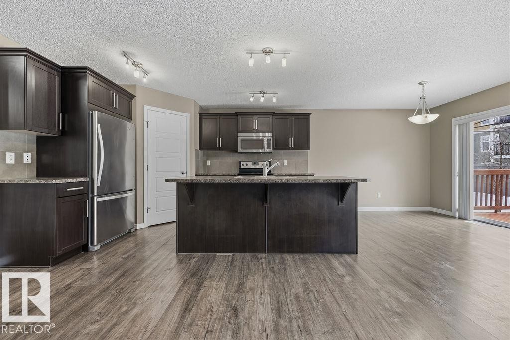 The kitchen features dark wood cabinetry, stainless steel appliances, a dark countertop, and a kitchen island with a sink - 7873 170A Avenue, Edmonton, AB - Indoor Photo Showing Kitchen With Stainless Steel Kitchen With Upgraded Kitchen