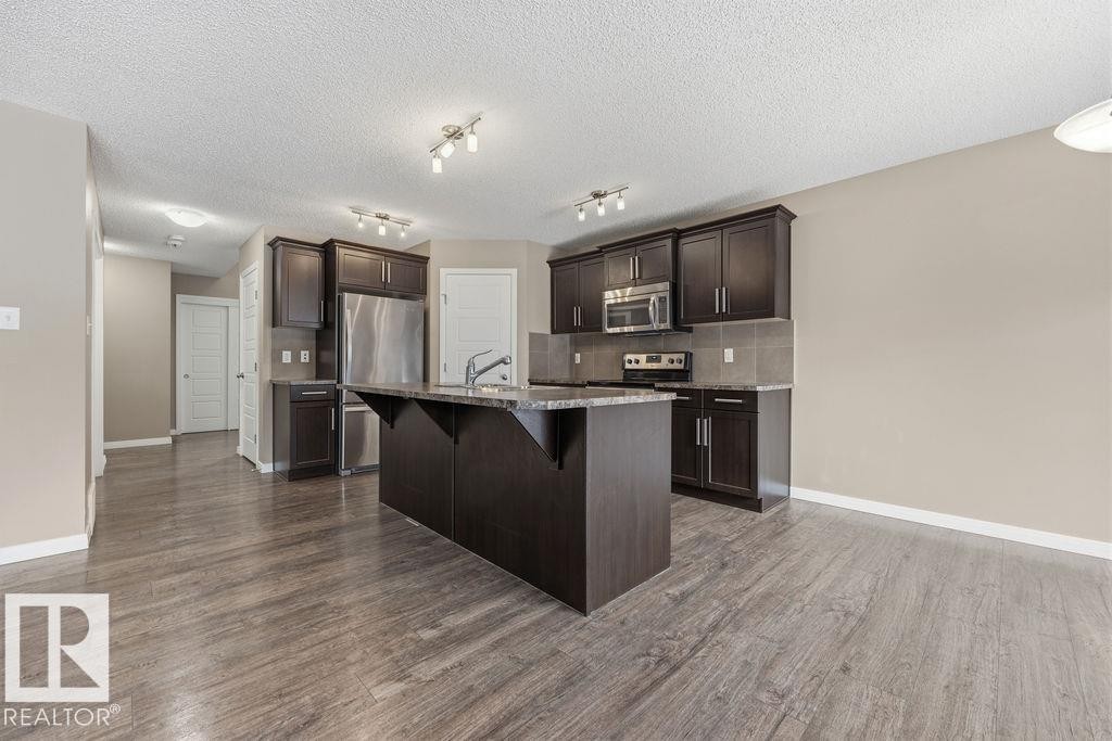 Spacious open-concept kitchen featuring dark wood cabinetry, granite countertops, stainless steel appliances, and a large central island - 7873 170A Avenue, Edmonton, AB - Indoor Photo Showing Kitchen